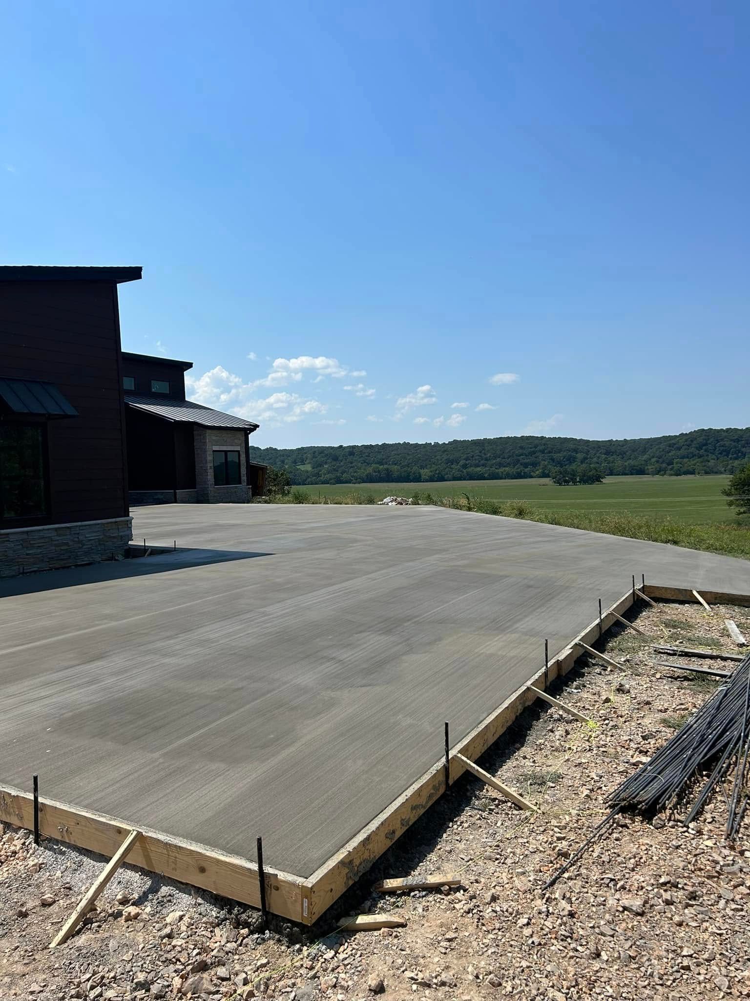 Concrete patio beside a dark wooden building, overlooking a grassy field under a clear blue sky