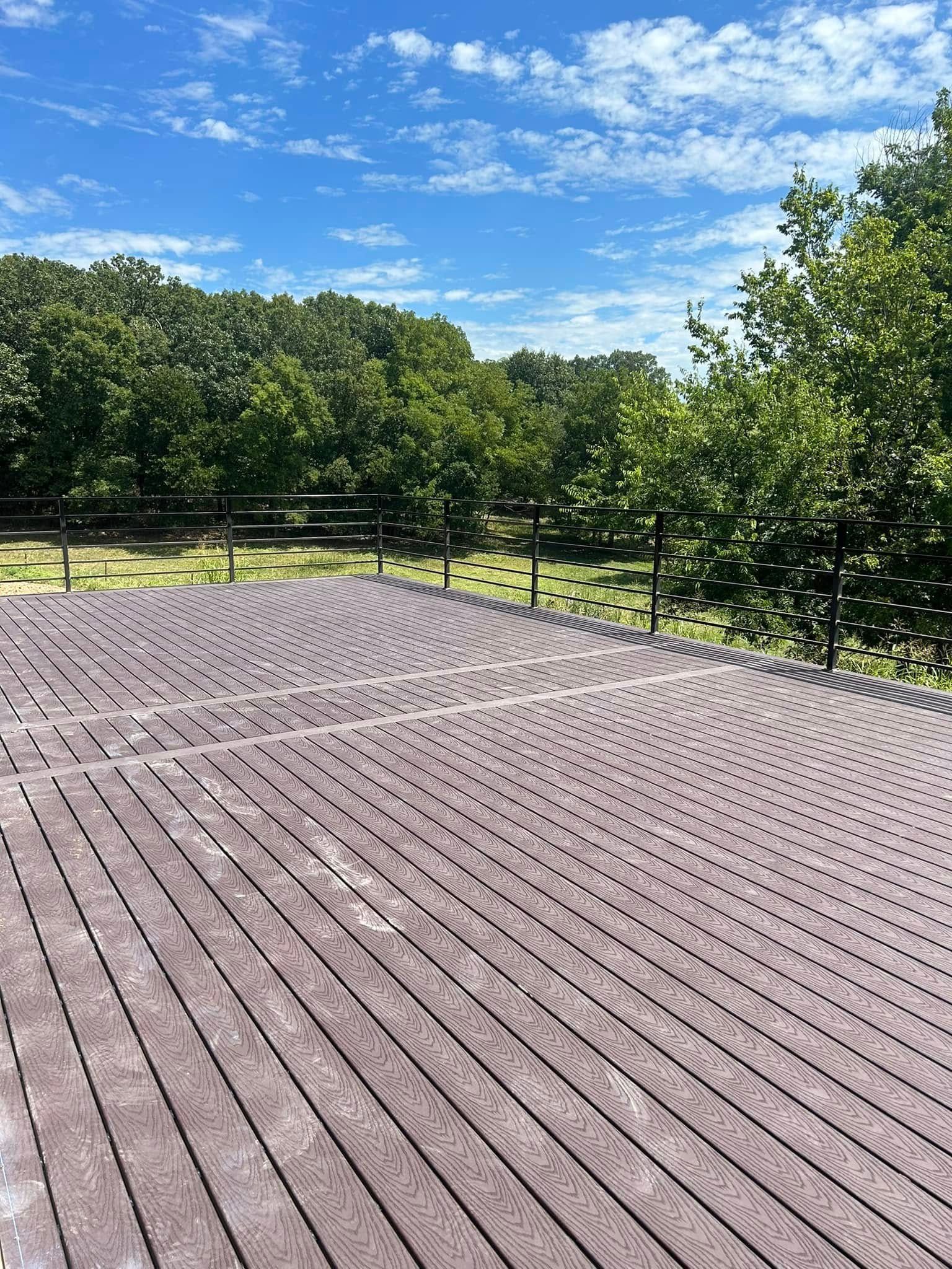 Wooden deck overlooking green trees under a bright blue, partly cloudy sky
