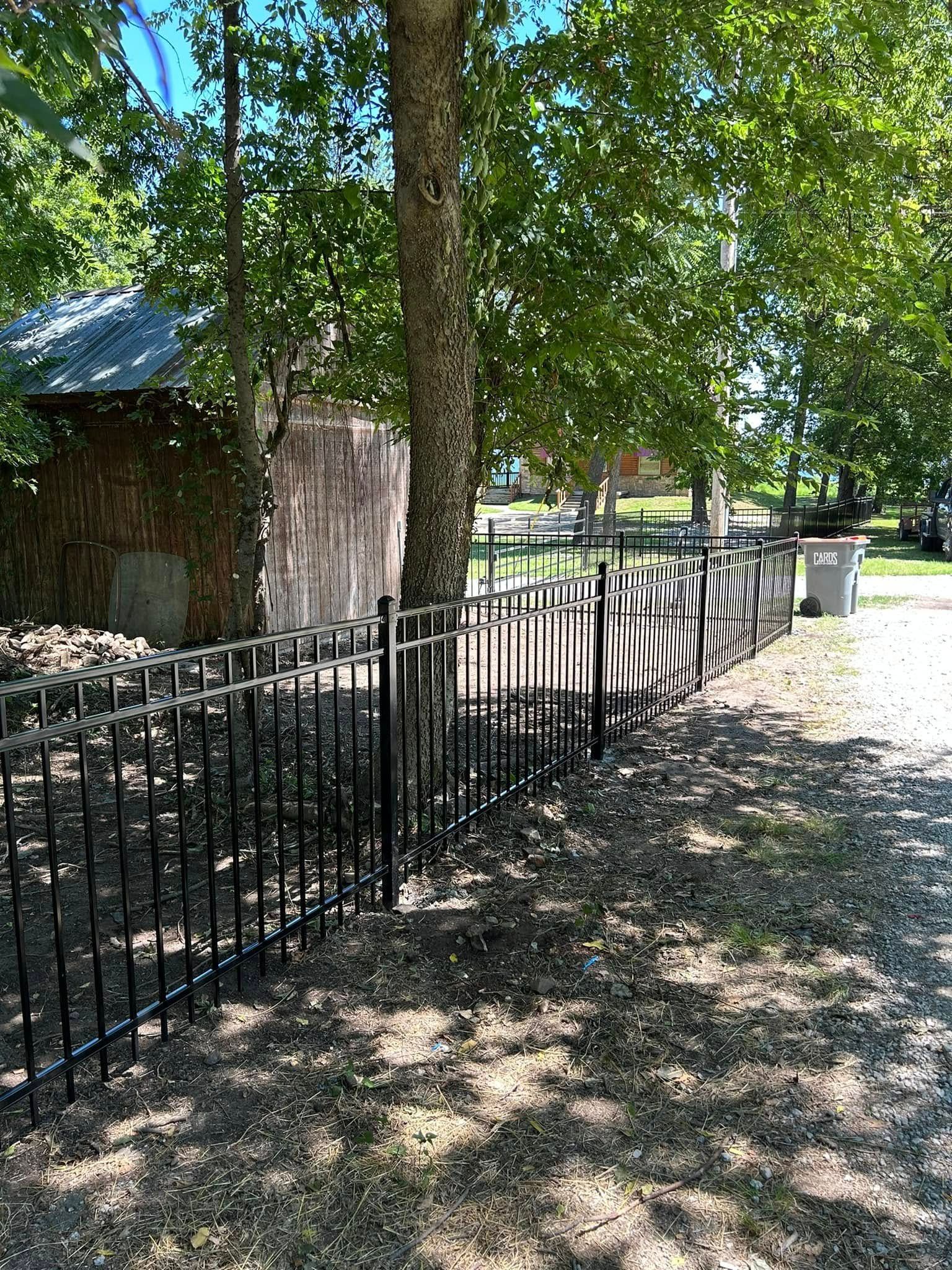 Shaded park path beside a black iron fence and trees on a sunny day