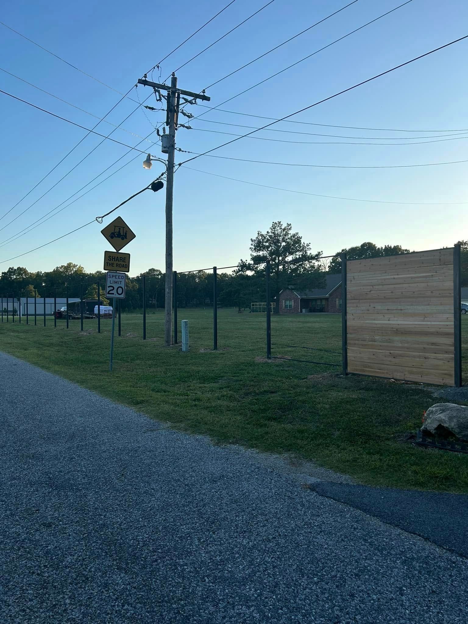 Gravel road beside a fenced field at dusk, with a utility pole and warning signs