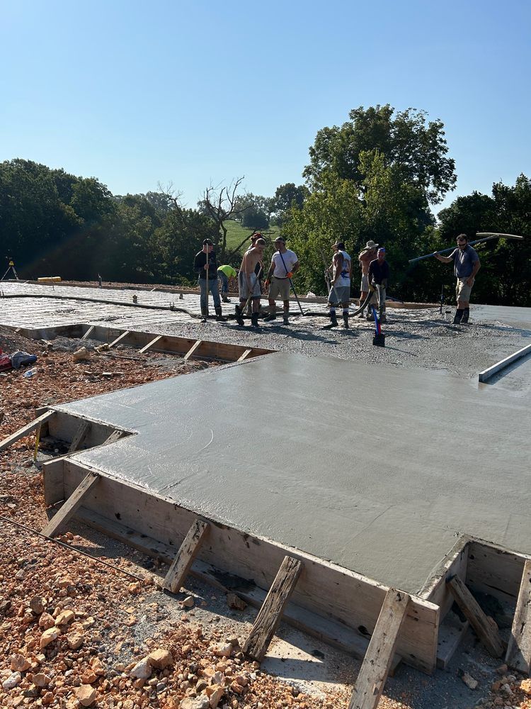 Workers standing on a newly poured concrete slab at an outdoor construction site under a clear sky