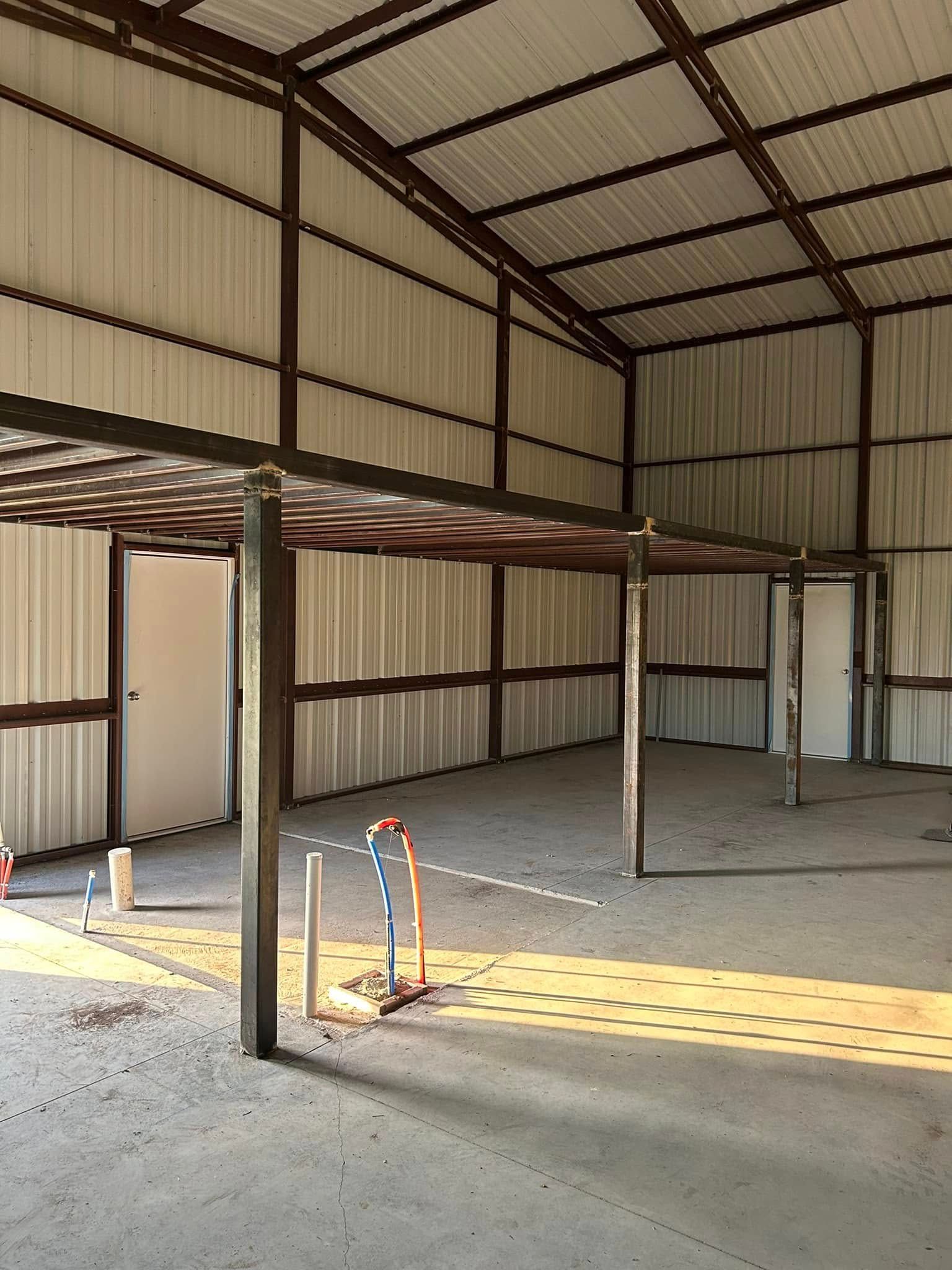 Empty industrial warehouse with metal beams, corrugated walls, and a concrete floor.