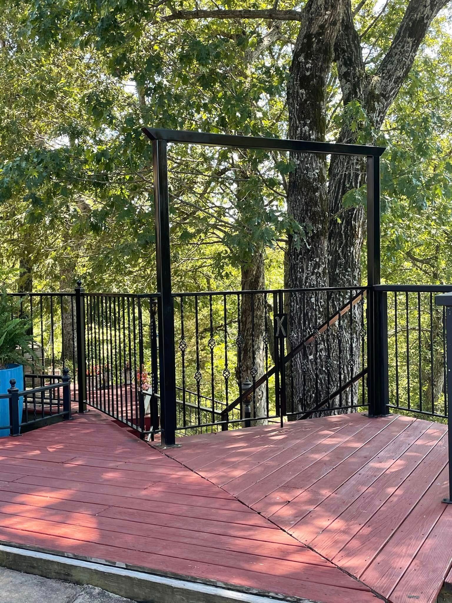 Wooden deck with black railing and stairs overlooking a leafy wooded area
