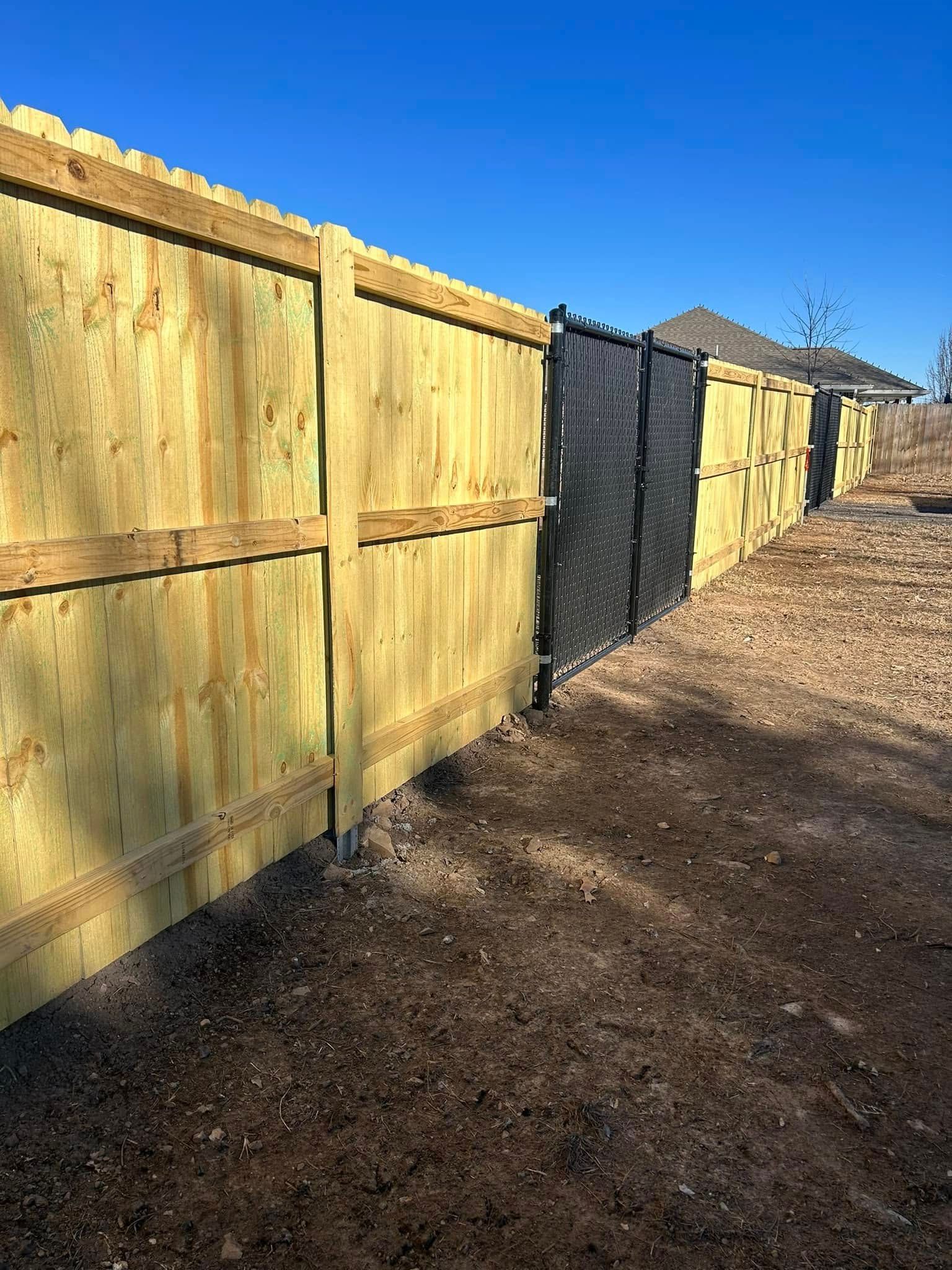 Wooden backyard fence along a dirt path under a clear blue sky