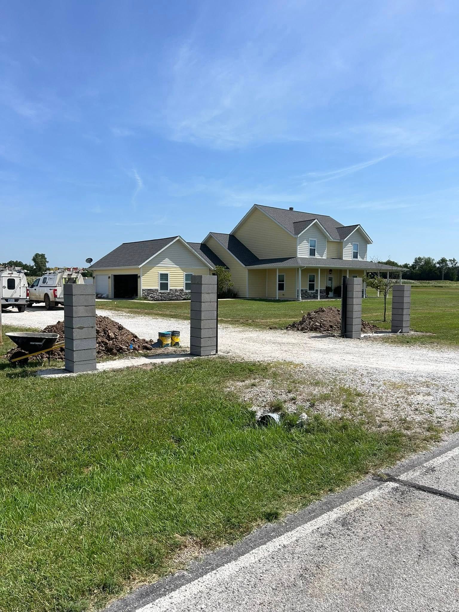 Partially built house with gray roof on a gravel lot beside a road, under a clear blue sky