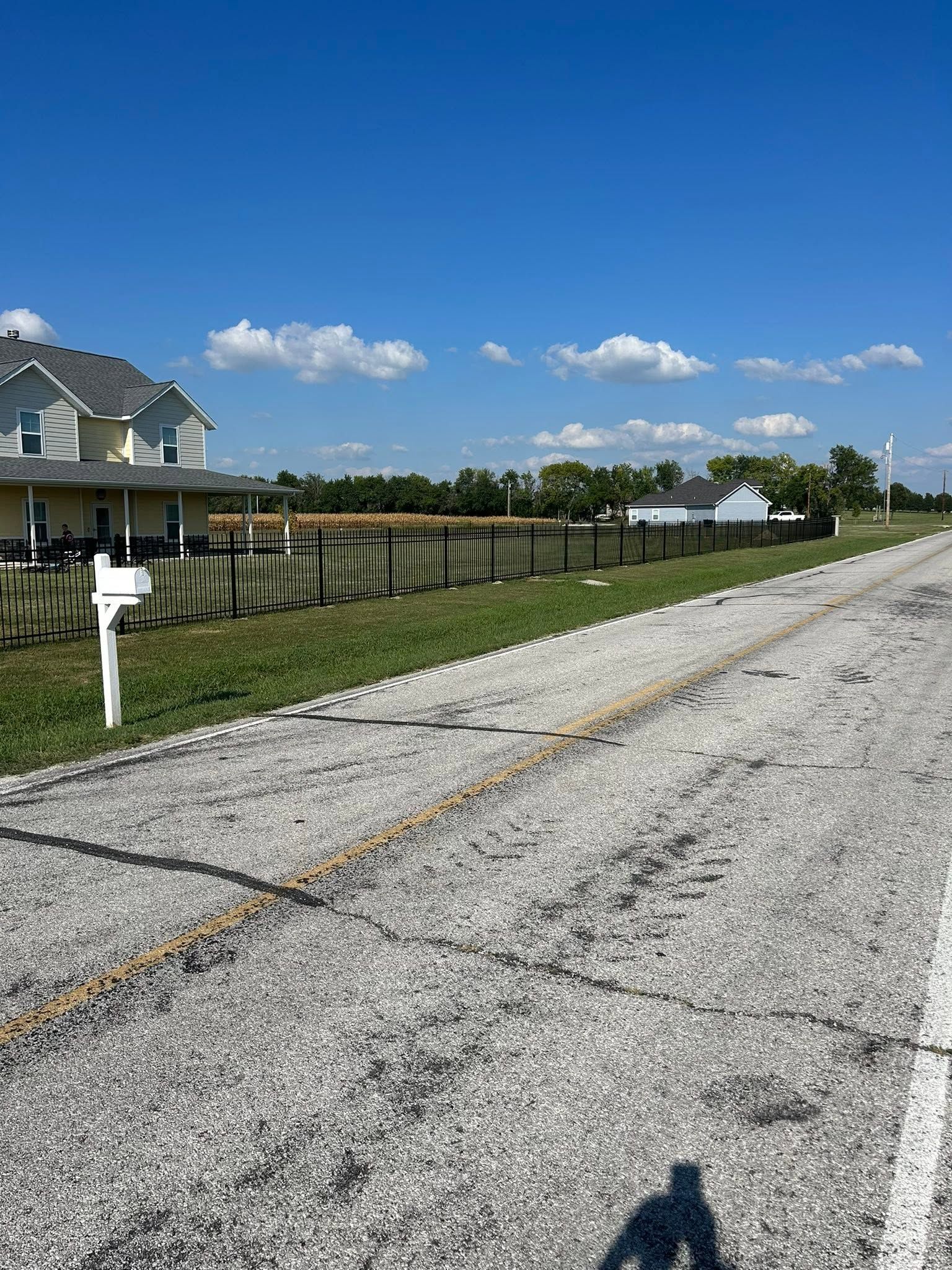 Empty suburban street beside a fenced row of houses under a bright blue sky with clouds