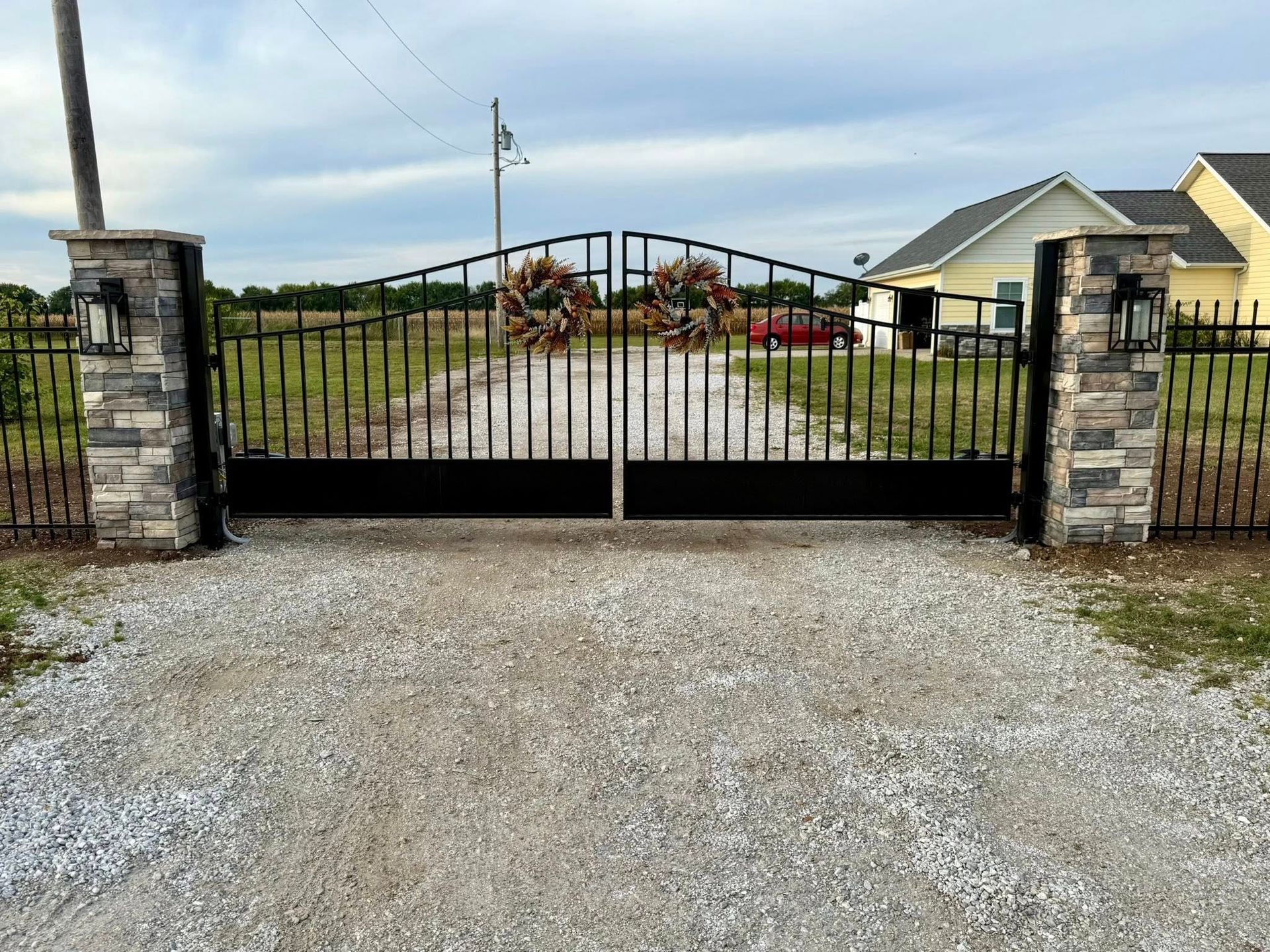 Closed black gate between stone pillars at the entrance of a gravel driveway to a house