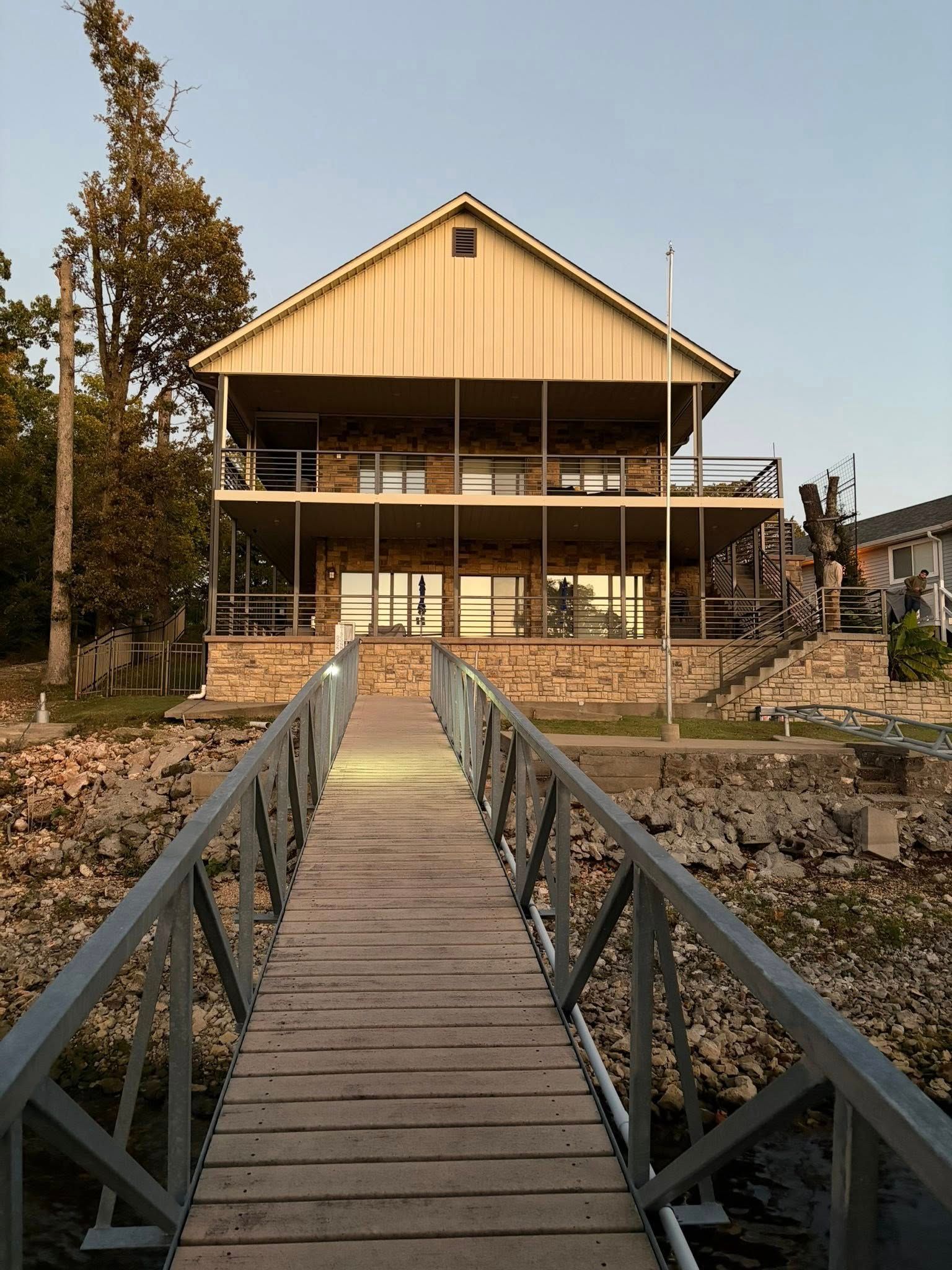 Wooden walkway leading to a large tan cabin by the water at sunset.