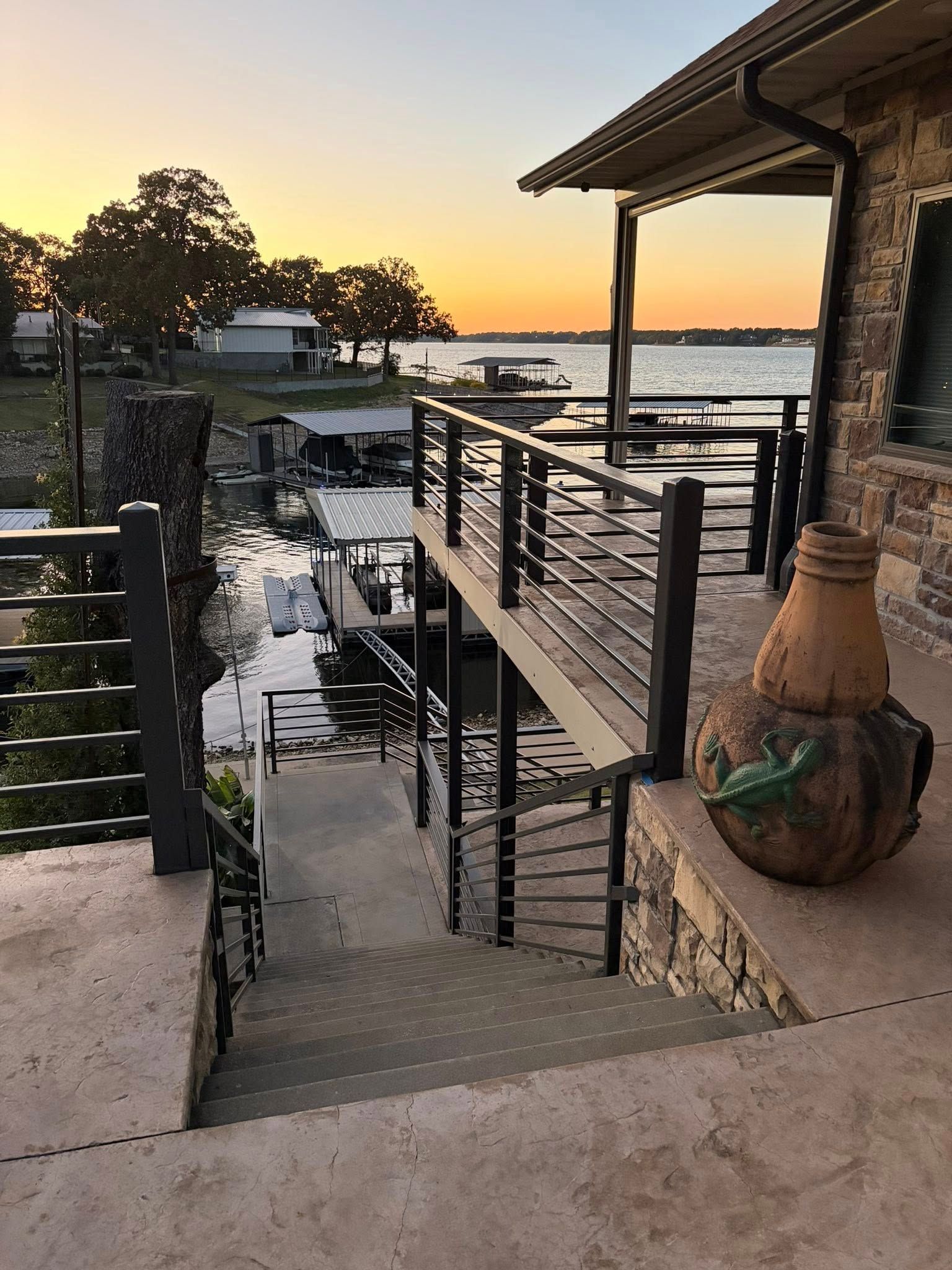 Sunset view of a waterfront patio with stairs, railing, and stone decor overlooking the water