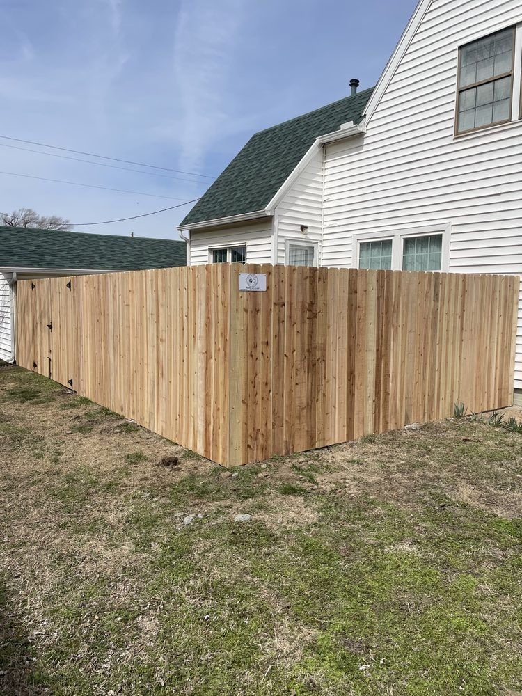 Freshly built wooden privacy fence beside a white house on a grassy yard under a blue sky