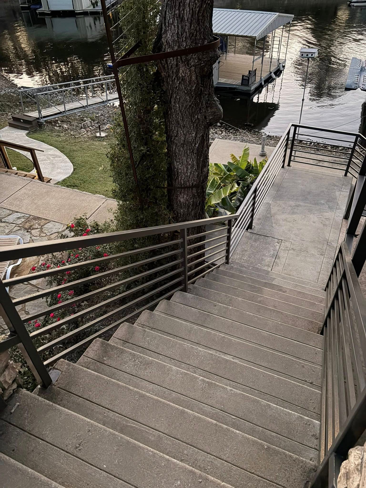 Steep outdoor stairs leading down to a waterfront walkway with railings and trees nearby