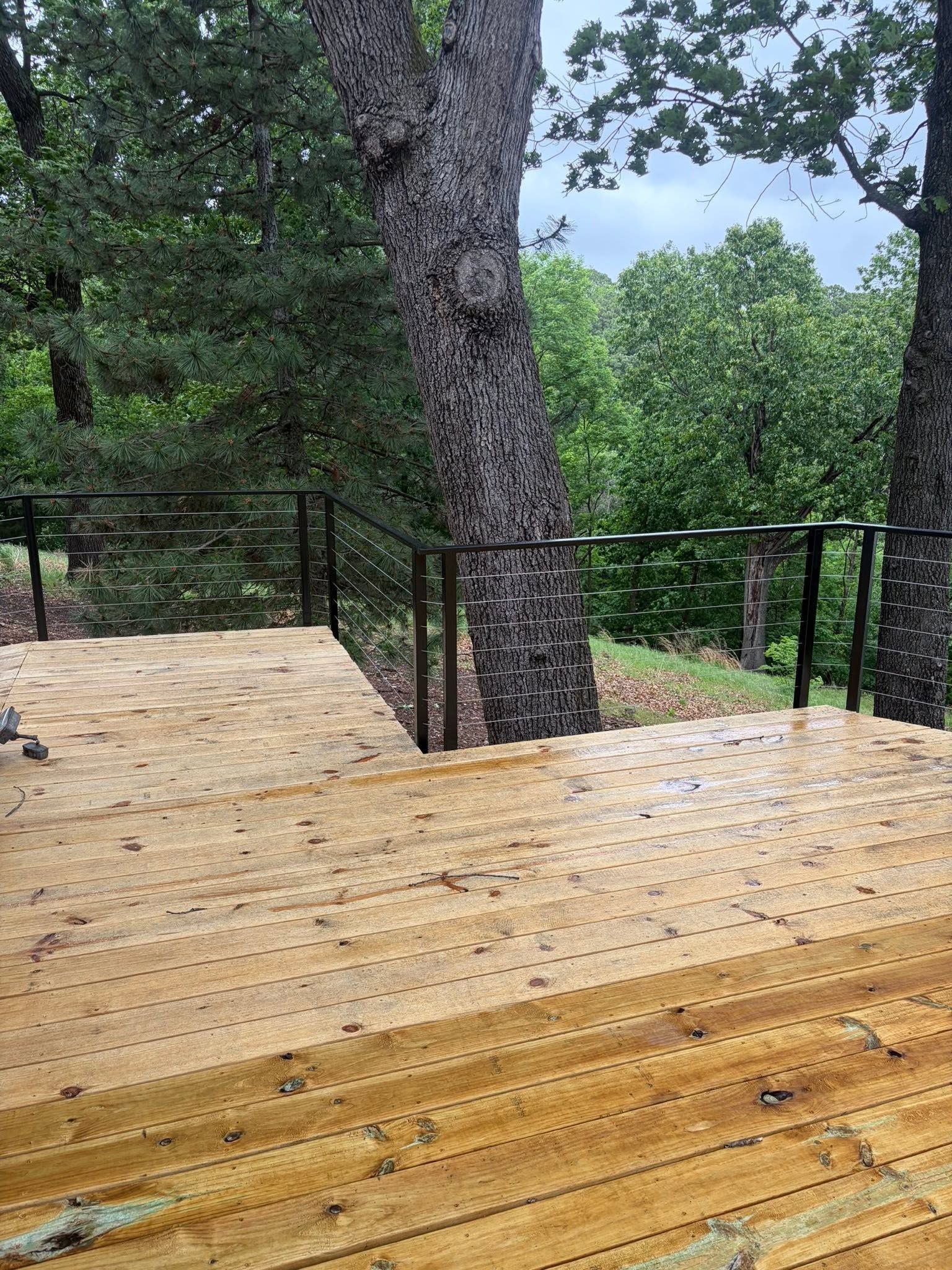 Wooden deck overlooking a green wooded area, with a large tree trunk in the center.