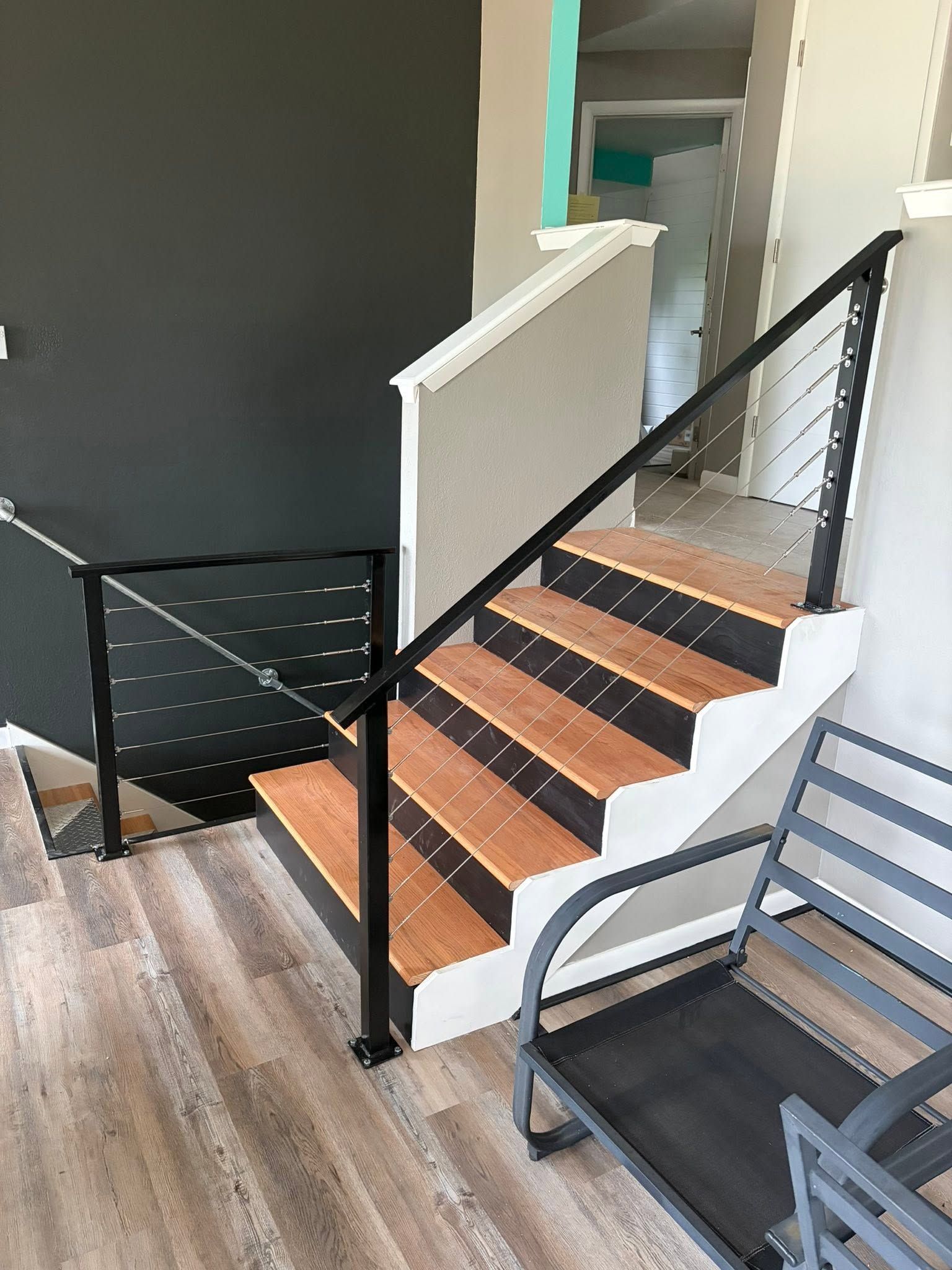 Indoor staircase with black handrail, wood steps, and gray flooring next to a dark wall