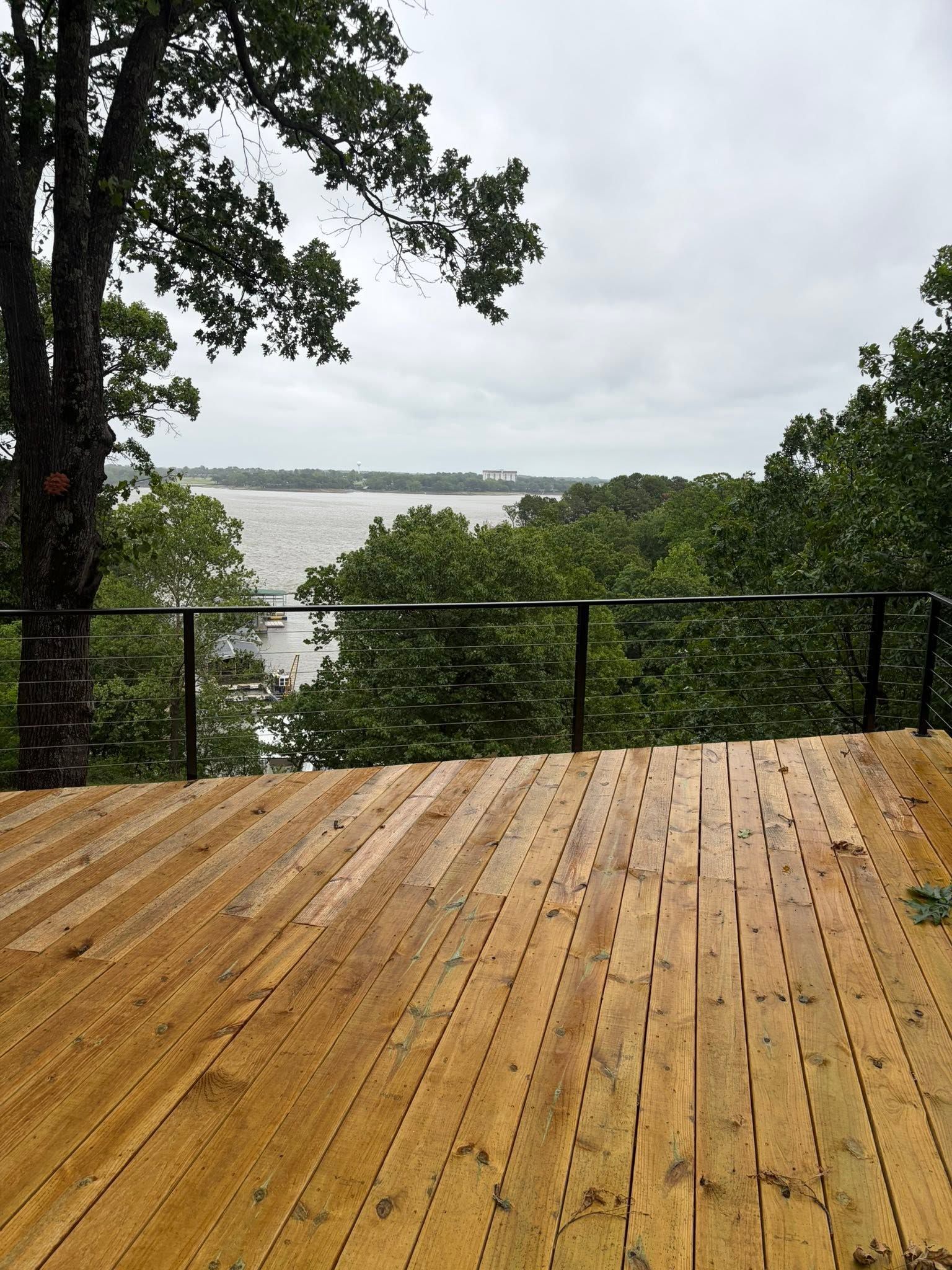 Rainy wooden deck overlooking a lake through trees and a black railing