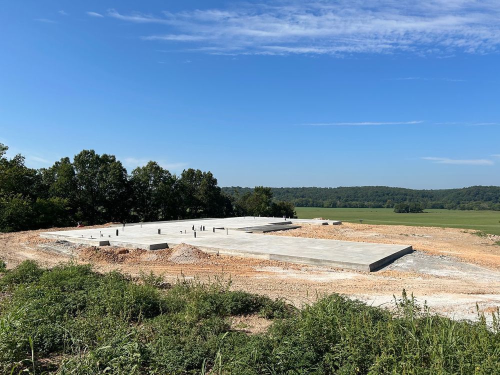 Concrete foundation slab under construction in a rural field beneath a clear blue sky