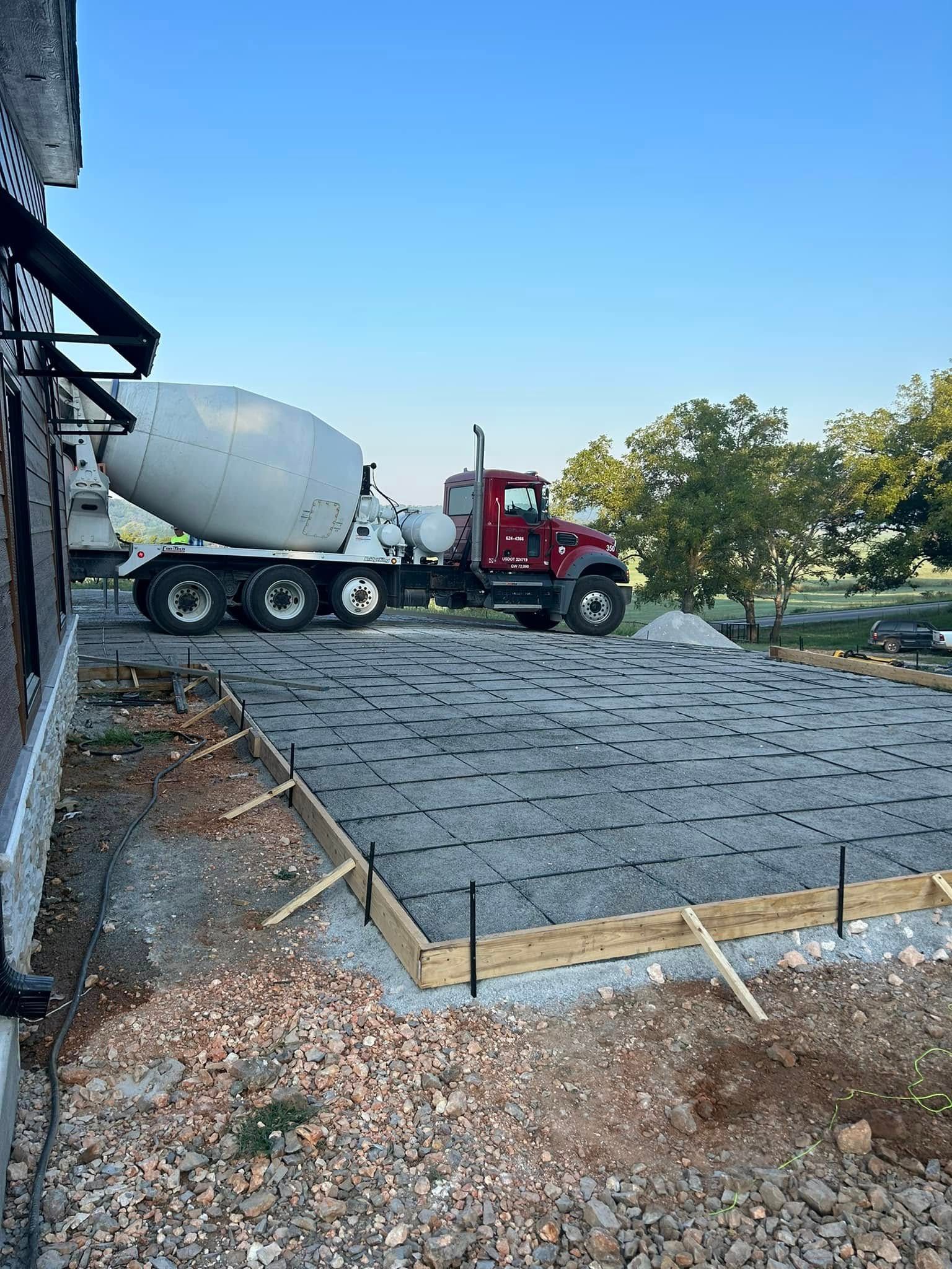Red concrete mixer truck pouring a slab beside a house under construction at sunset
