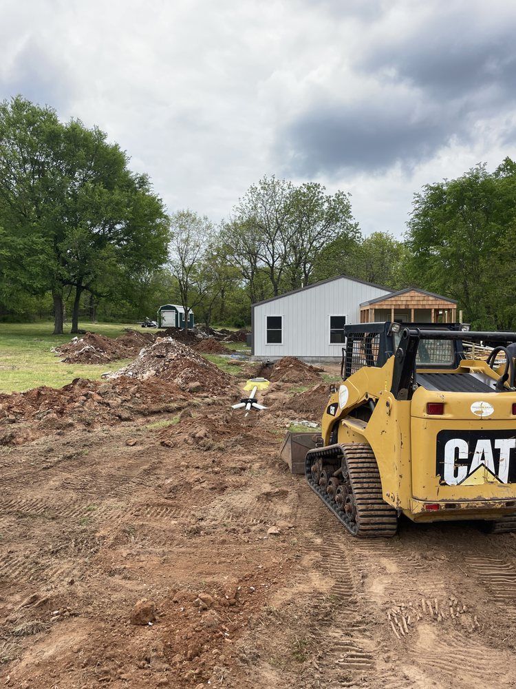 Yellow CAT skid steer on a dirt path at a construction site with trees and a white building in the background
