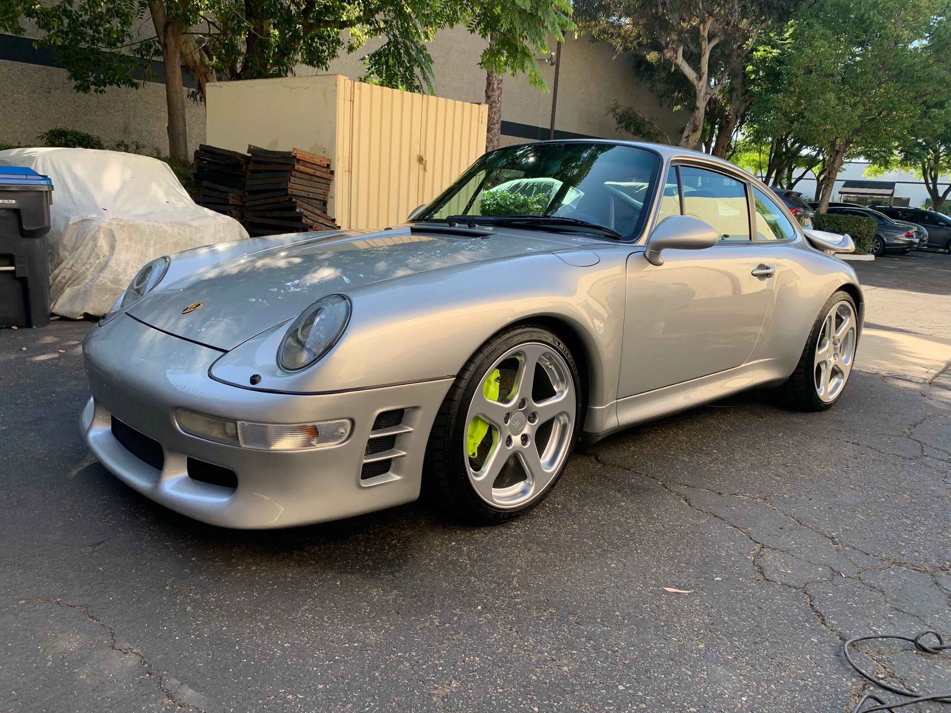 A bright blue Porsche Targa parked on a suburban driveway with a white car visible in the background.