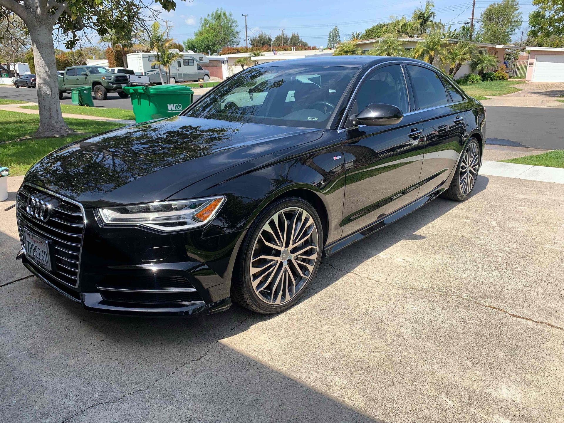 Black sedan parked in a driveway on a sunny residential street