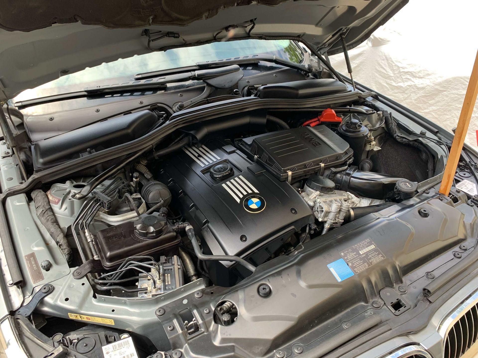 BMW engine bay with hood open, showing a black engine cover and surrounding components.