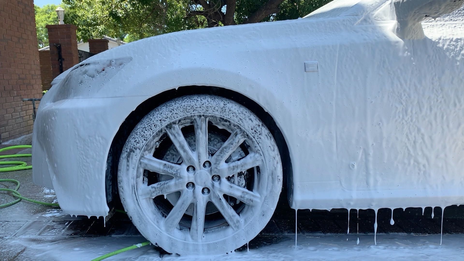 White car covered in foam during a car wash, with suds dripping over the wheels and body.