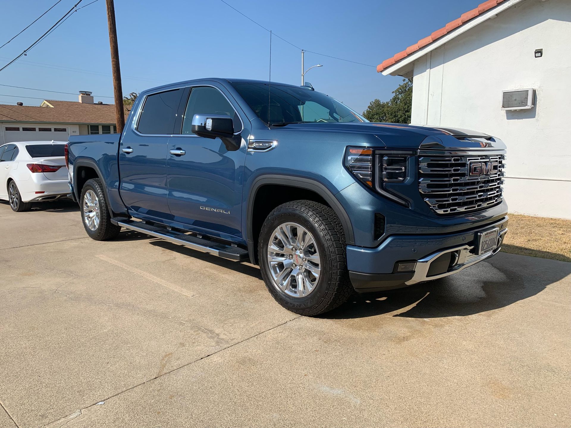 A blue GMC Sierra pickup truck parked on a concrete driveway next to a house.