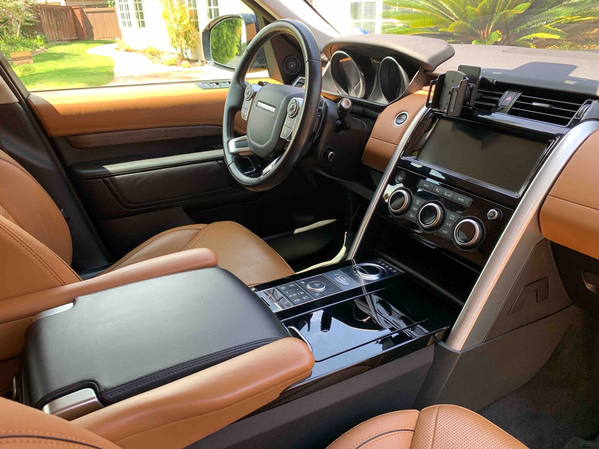 Luxury car interior with tan leather seats, black dashboard, and center console in daylight