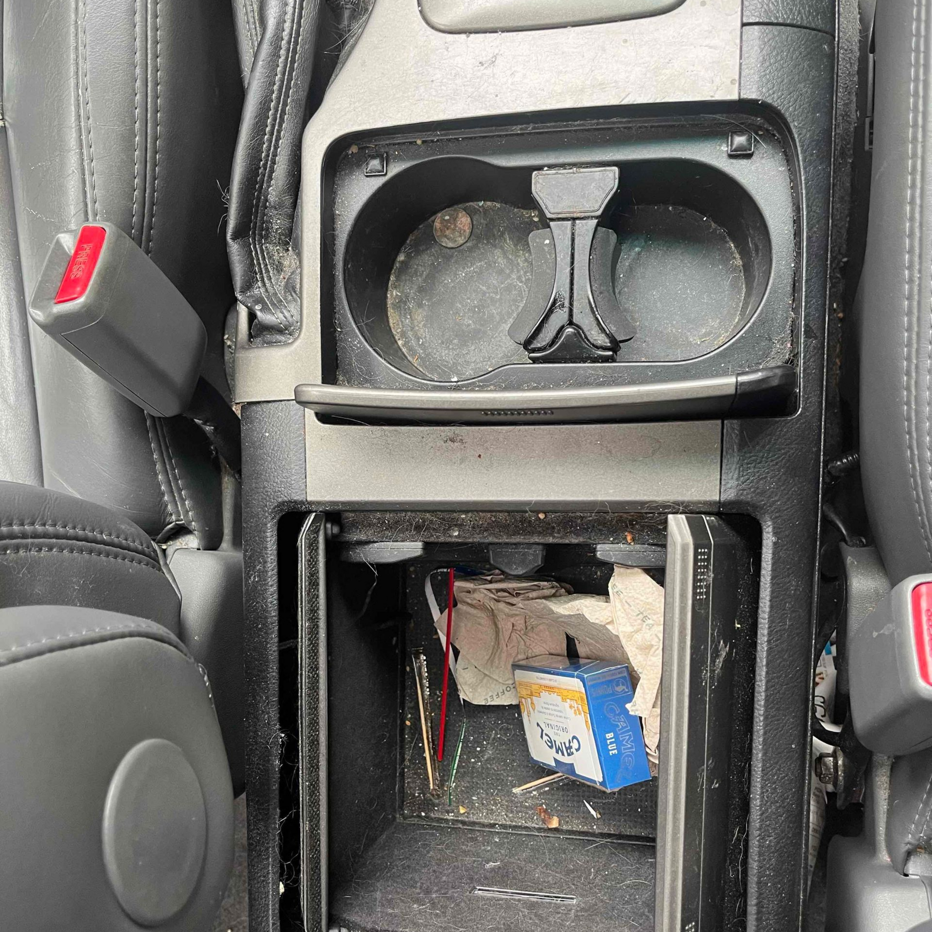 Car center console with cup holders, open storage compartment, and small items inside.