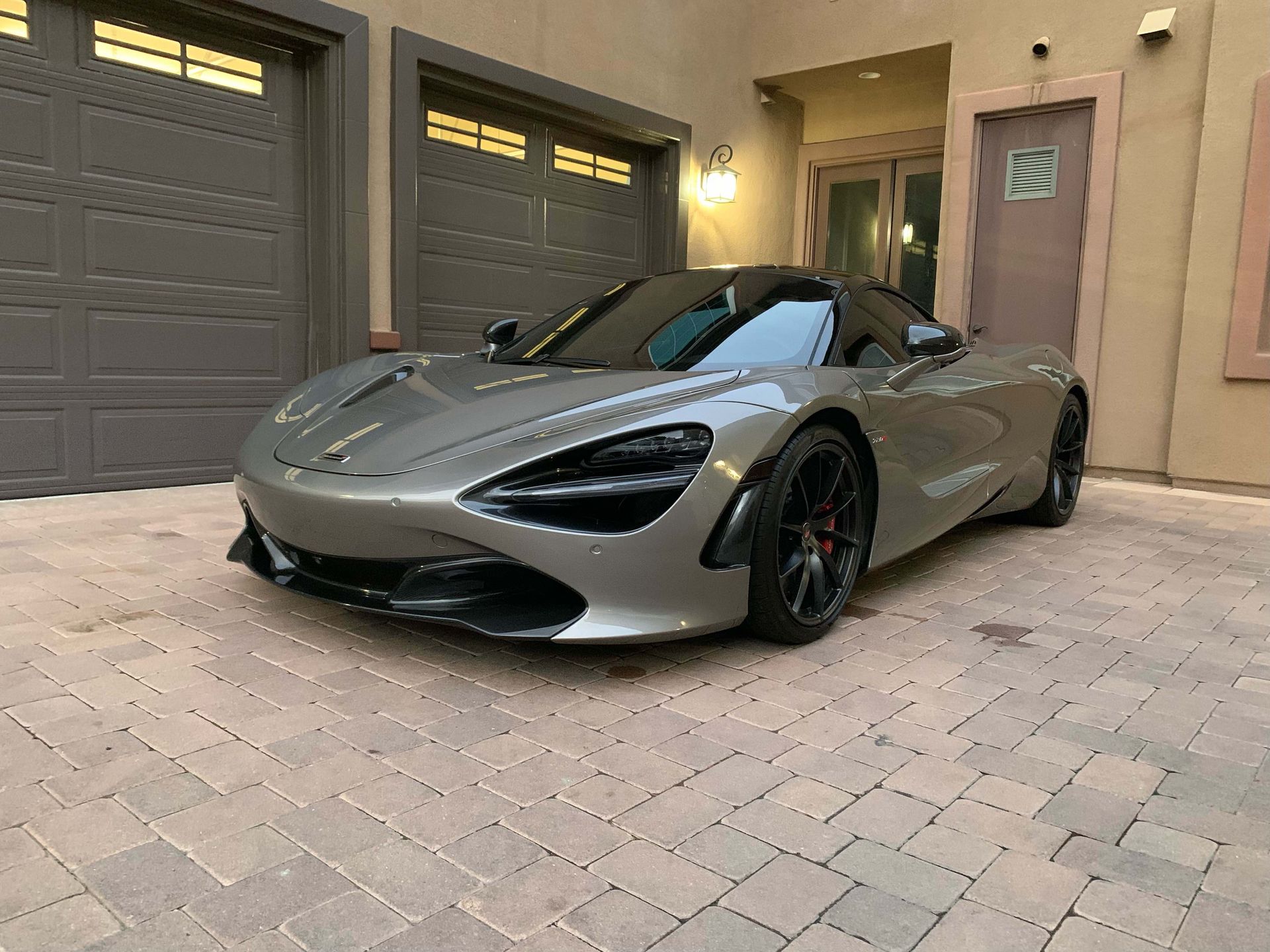 A grey McLaren sports car parked on a paved driveway in front of a garage.