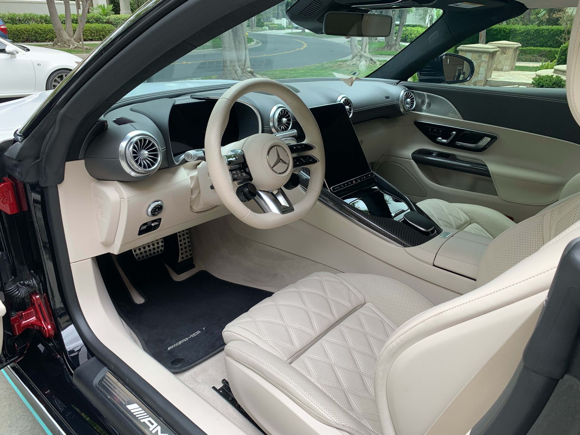 Luxury car interior with beige seats, white steering wheel, and glossy black center console.