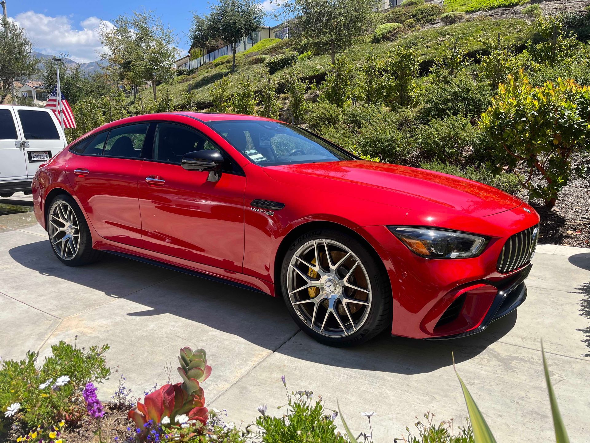 Red sports sedan parked on a sunny driveway beside greenery and flowers