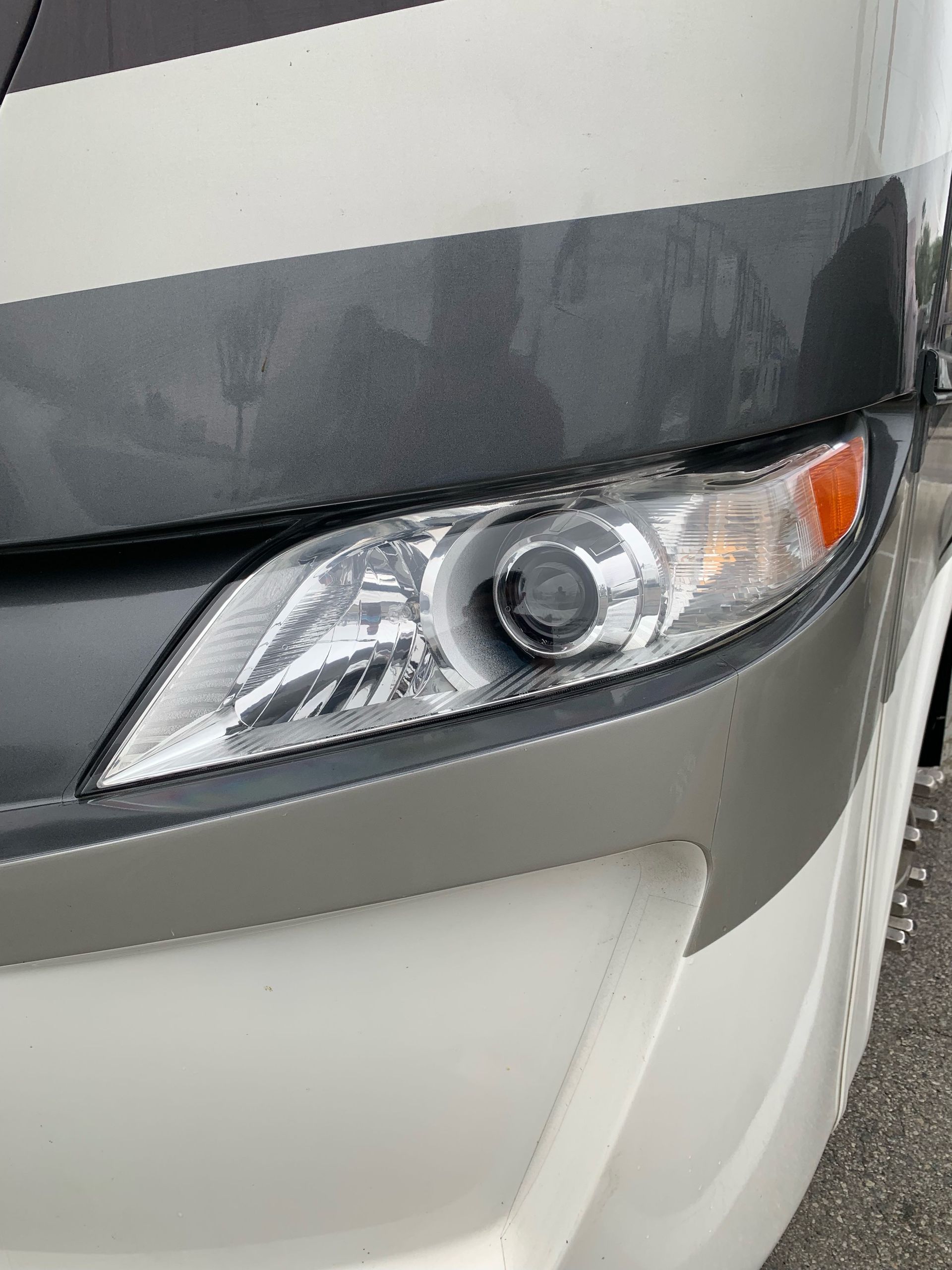 Close-up of a silver car’s front headlight and bumper on a dark background.