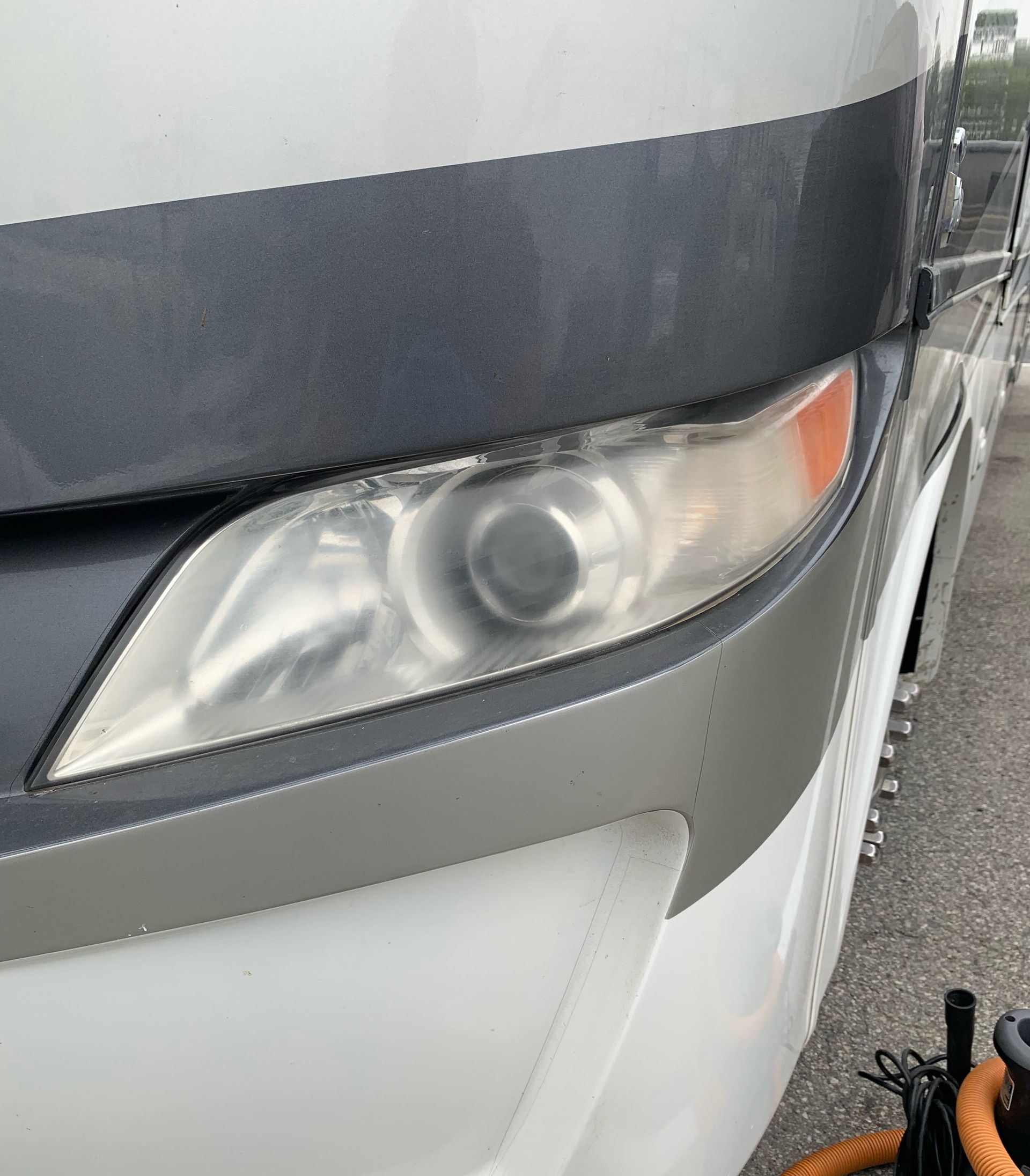 Close-up of a white and gray bus front with a headlight and orange turn signal.