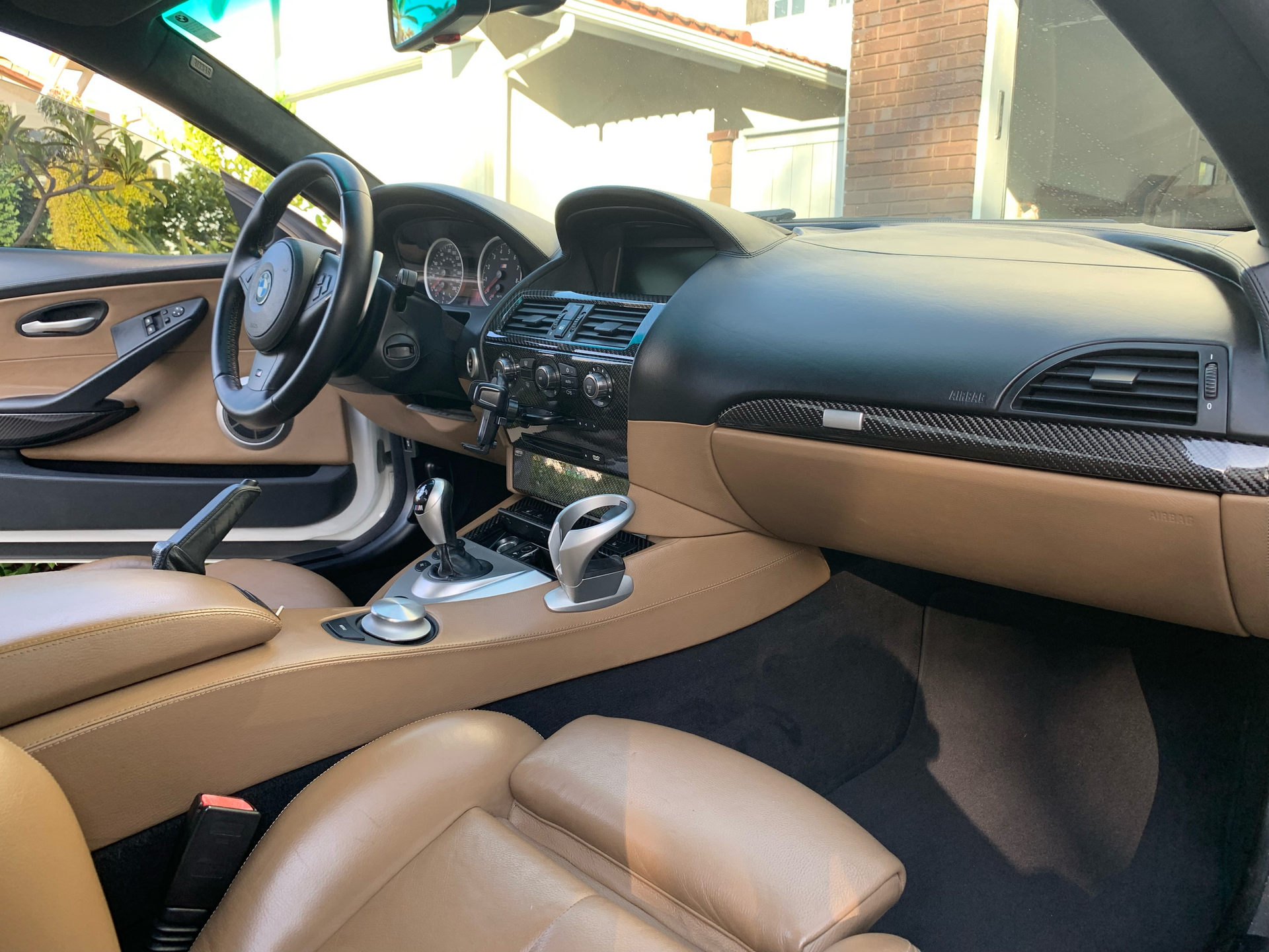 Tan leather car interior with black dashboard, center console, and steering wheel in sunlight