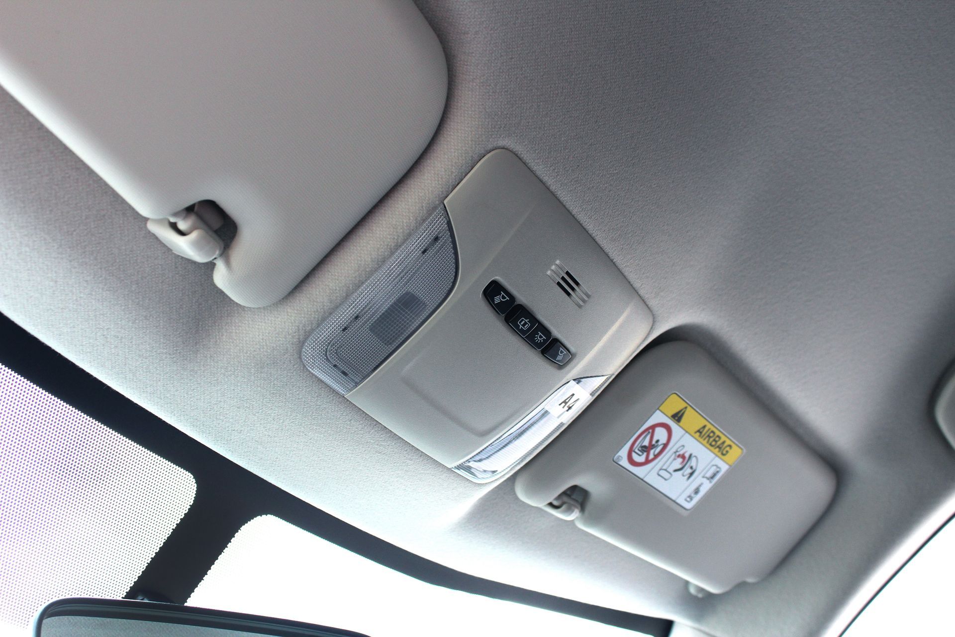 Car ceiling with overhead console, interior light, and safety warning label near the window