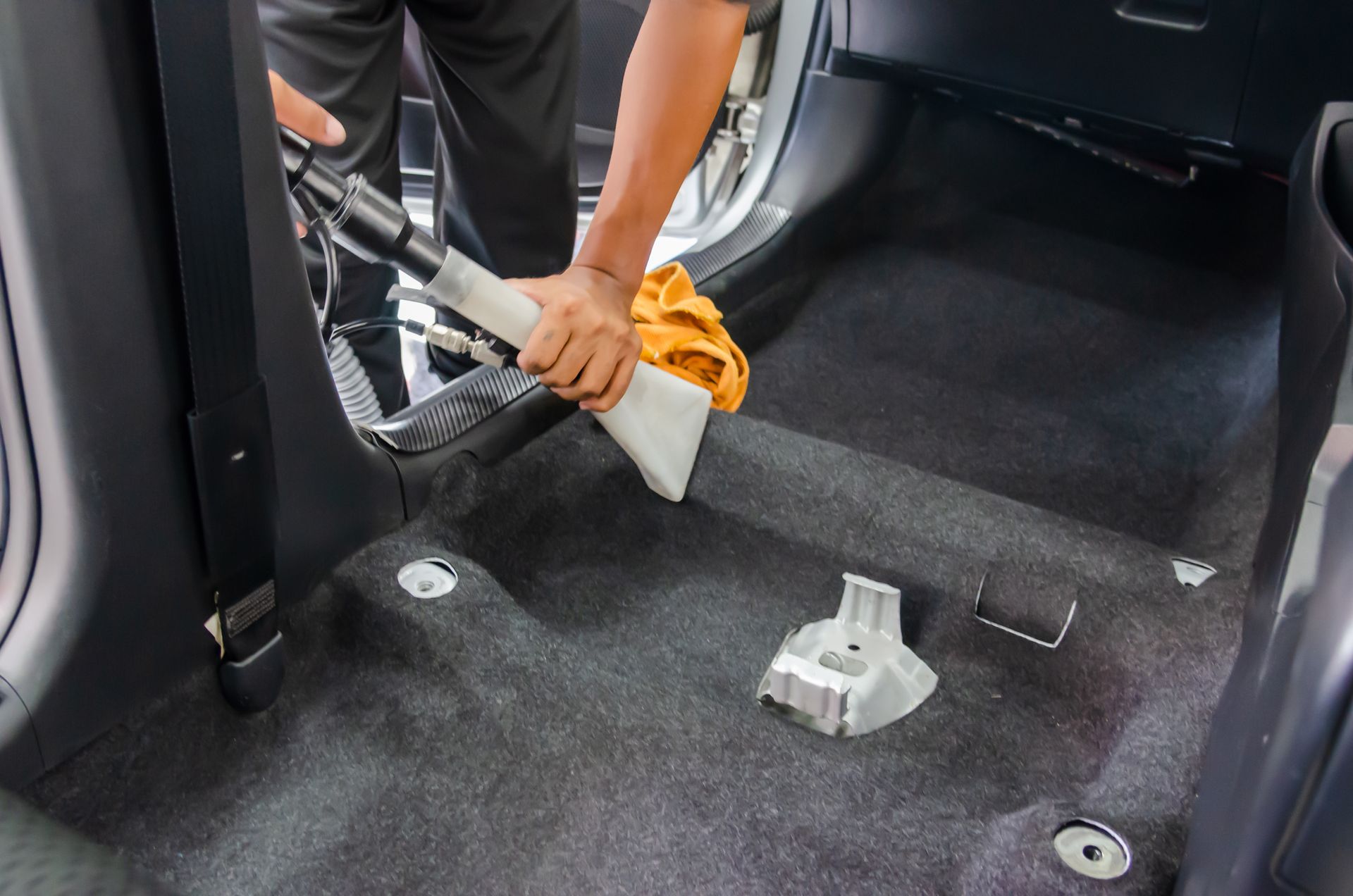 A person wearing black gloves cleans a black leather car seat.