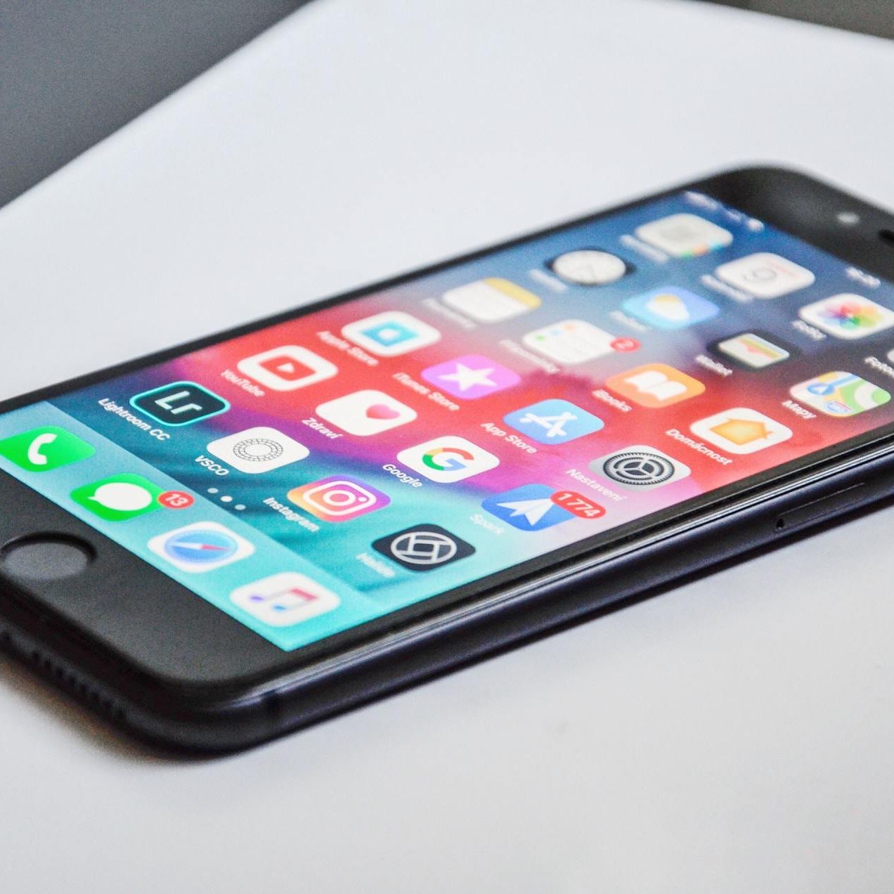 Black iPhone on a white surface, displaying app icons.