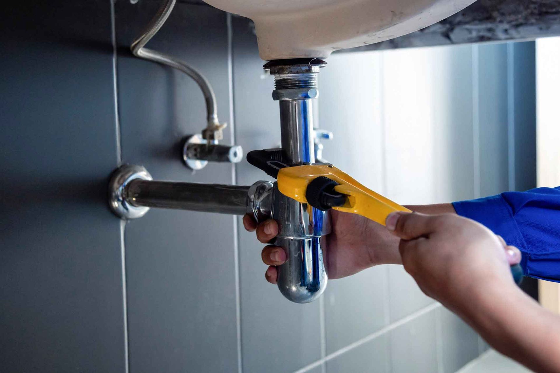 A plumber is fixing a sink pipe with a wrench.