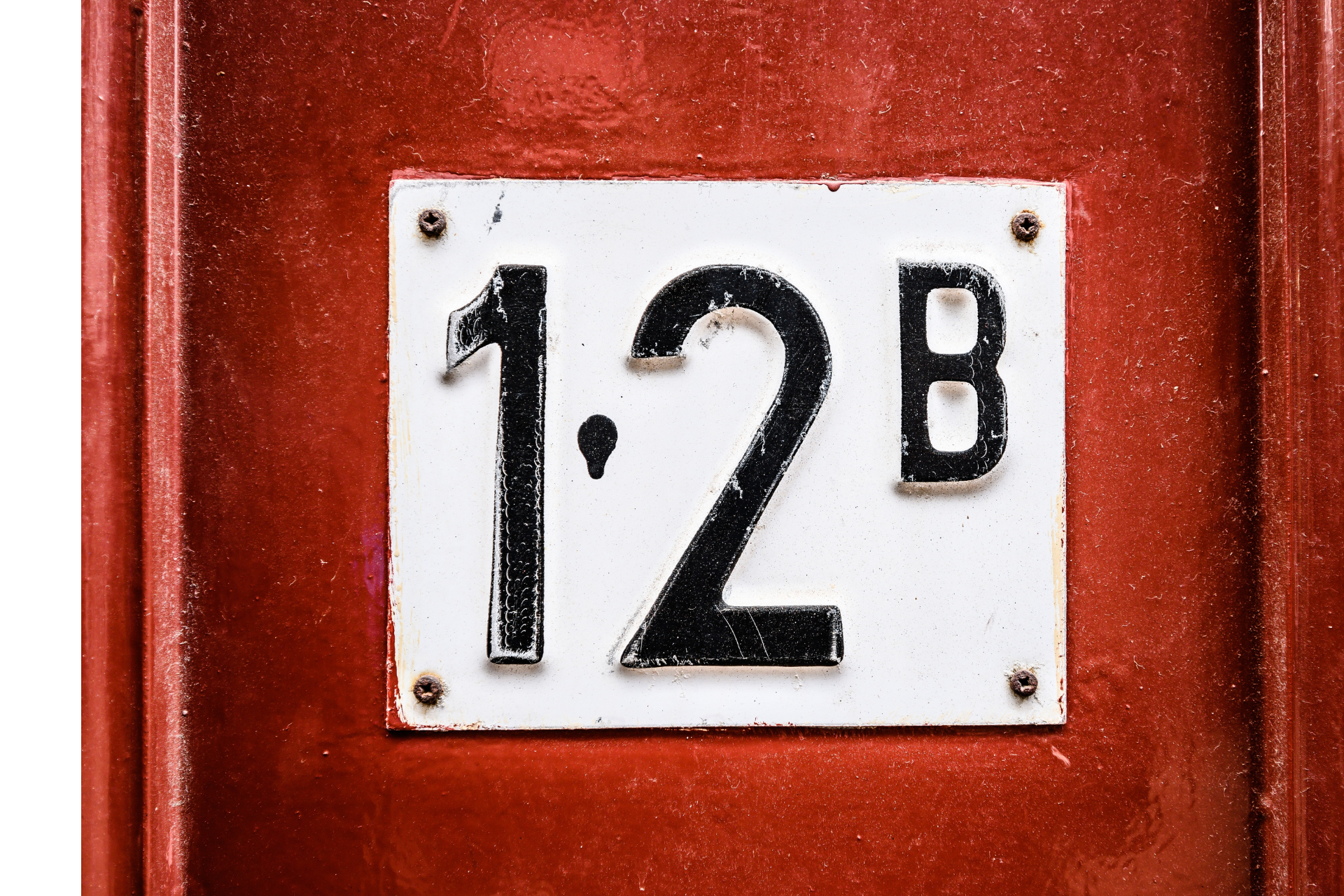 Witte plaquette met zwart huisnummer 12B op een rode muur