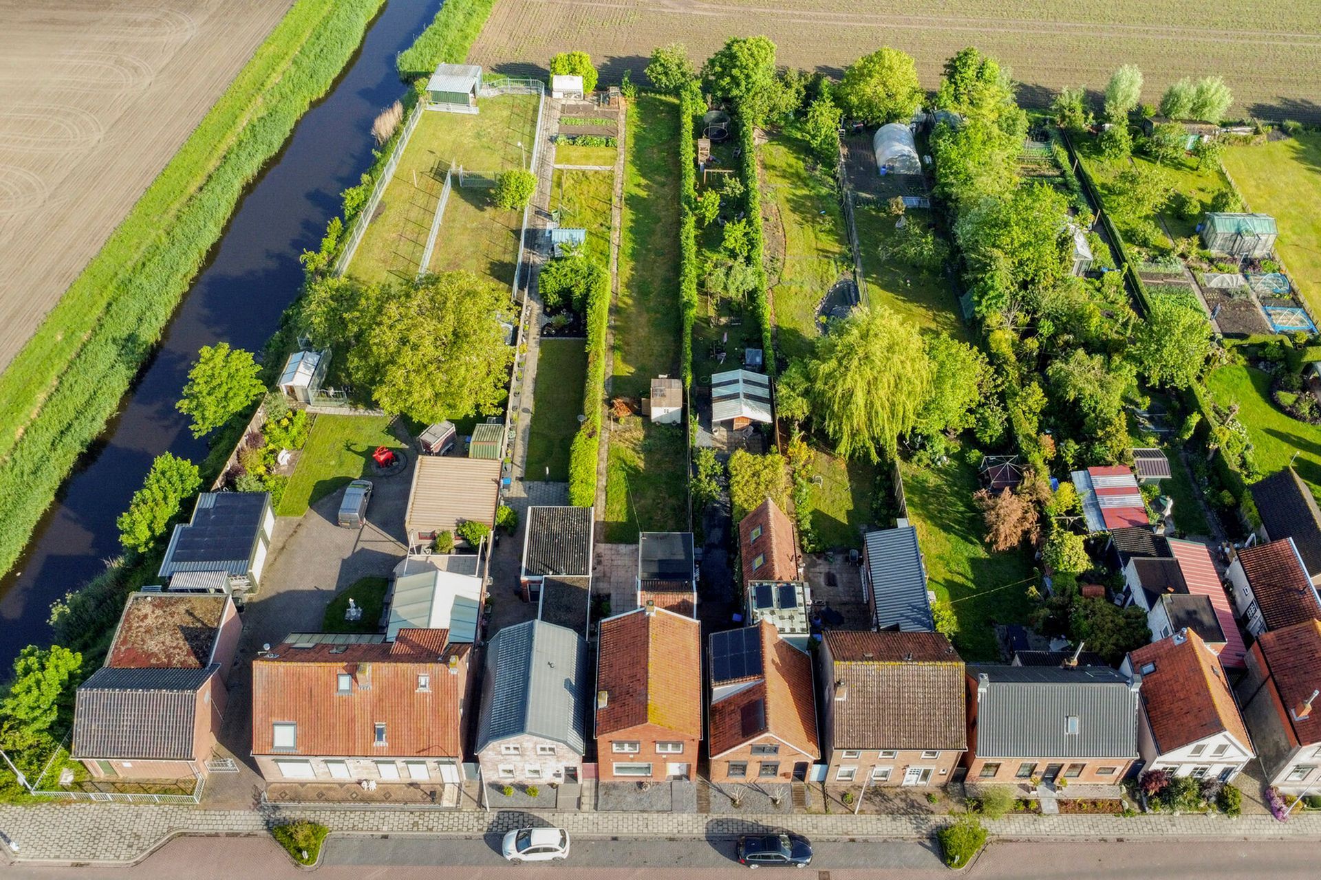 Terras in de achtertuin met bestrating, groen gazon en uitzicht op de huizen van de buren onder een blauwe hemel.