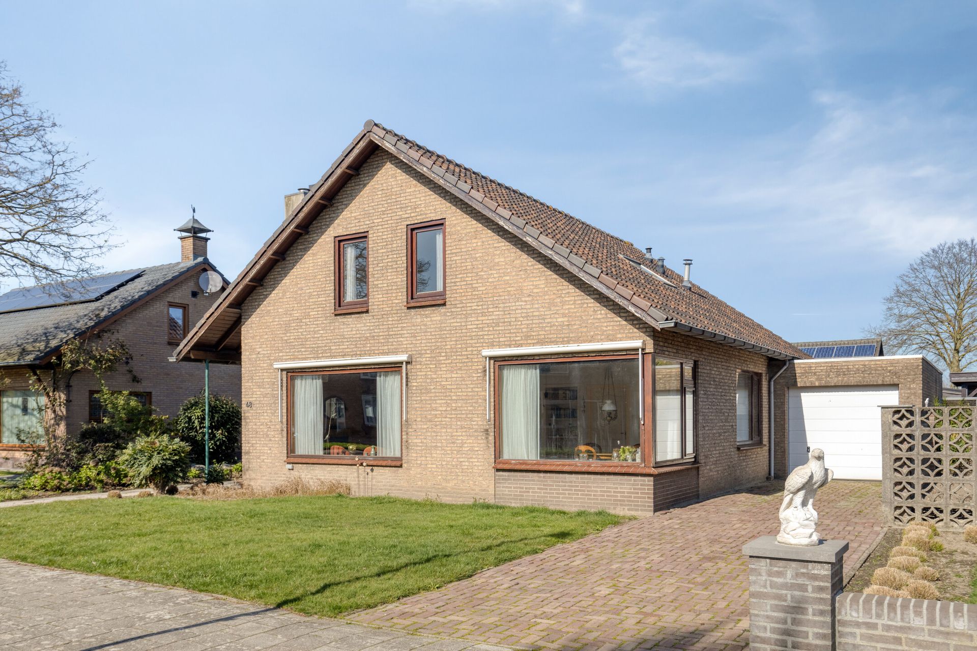 Bakstenen huis met steil dak, voortuin en oprit op een zonnige dag.
