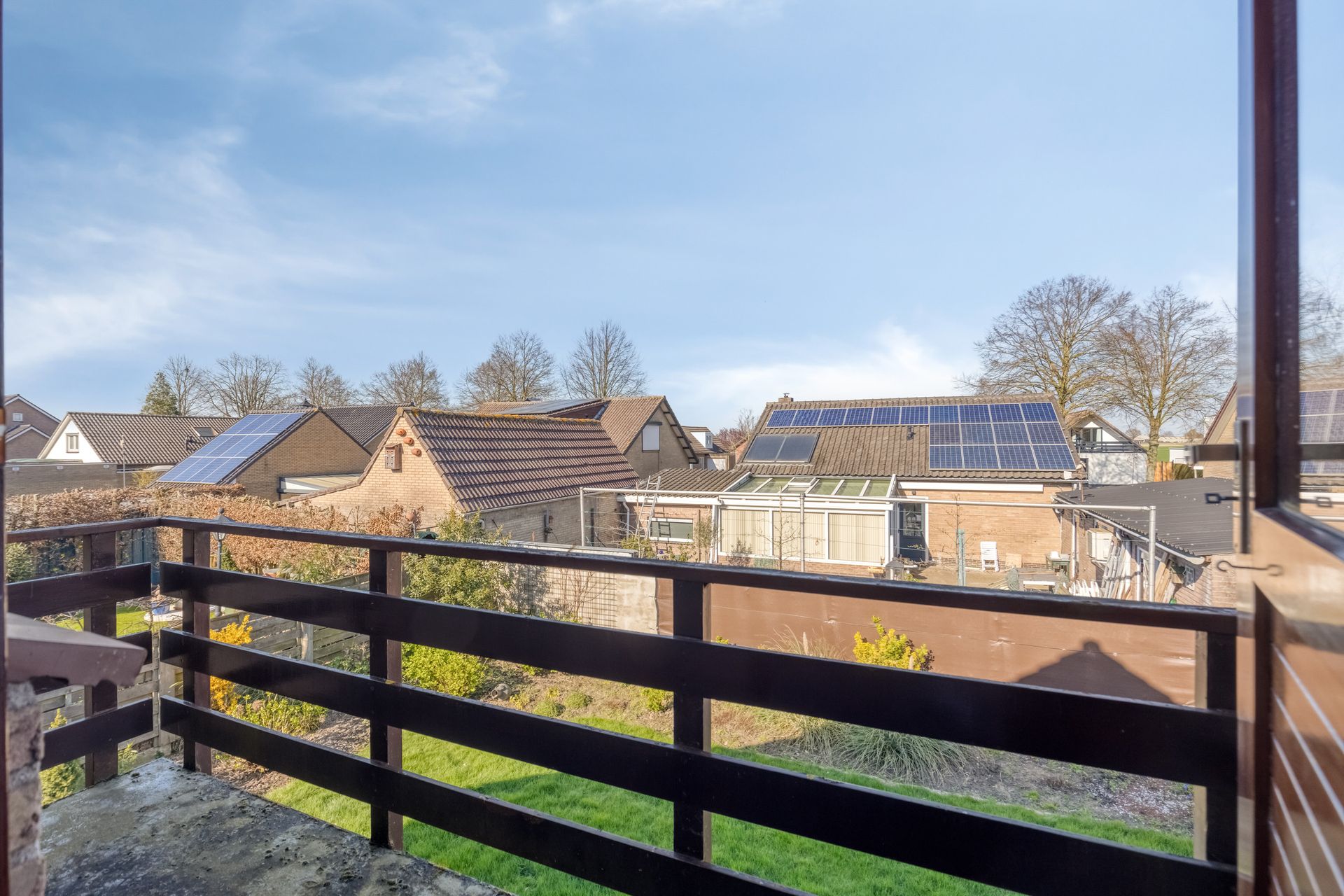 Uitzicht vanaf een balkon over daken en zonnepanelen op een zonnige dag.