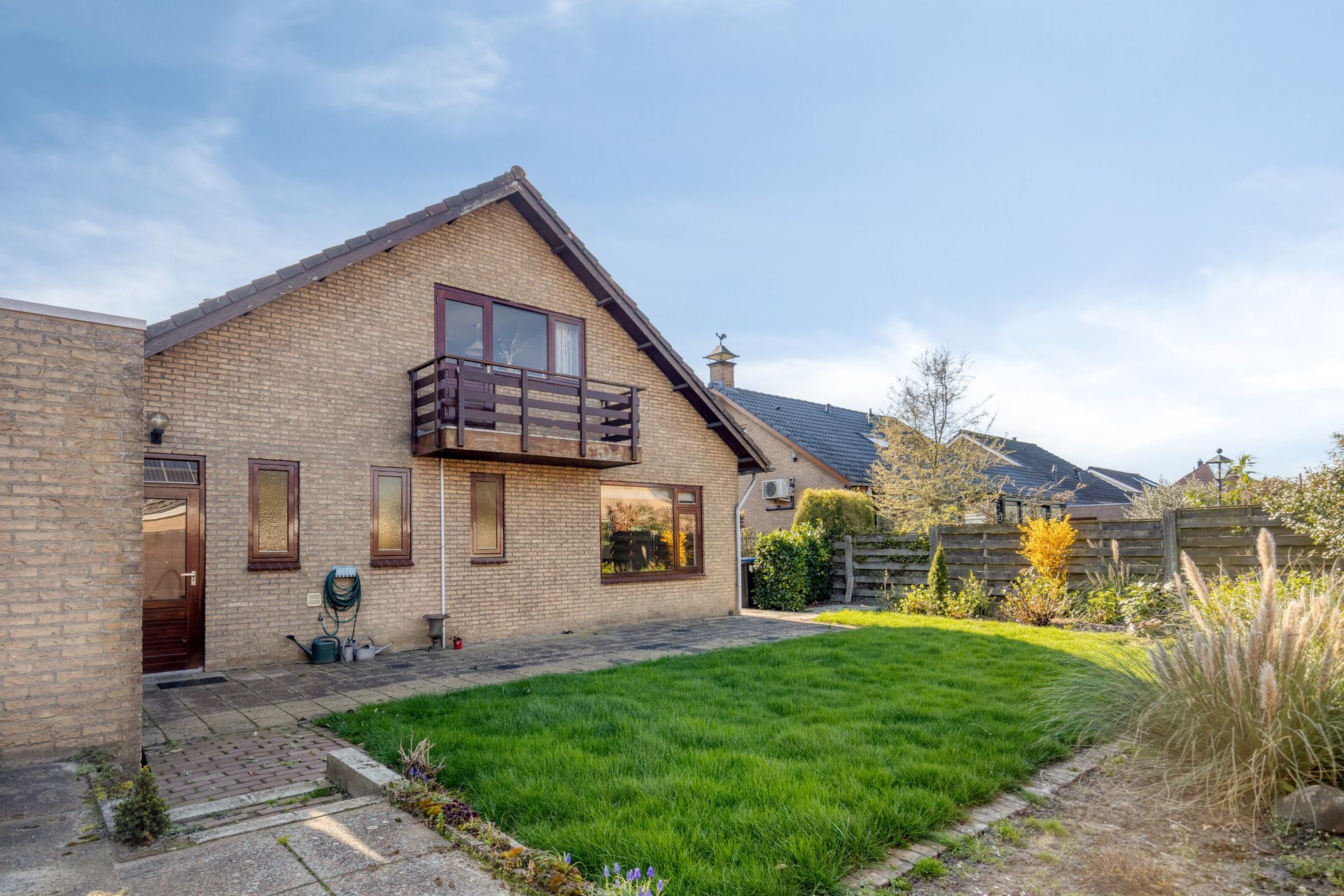 Bakstenen huis met balkon en groen gazon in een zonnige tuin in een buitenwijk.