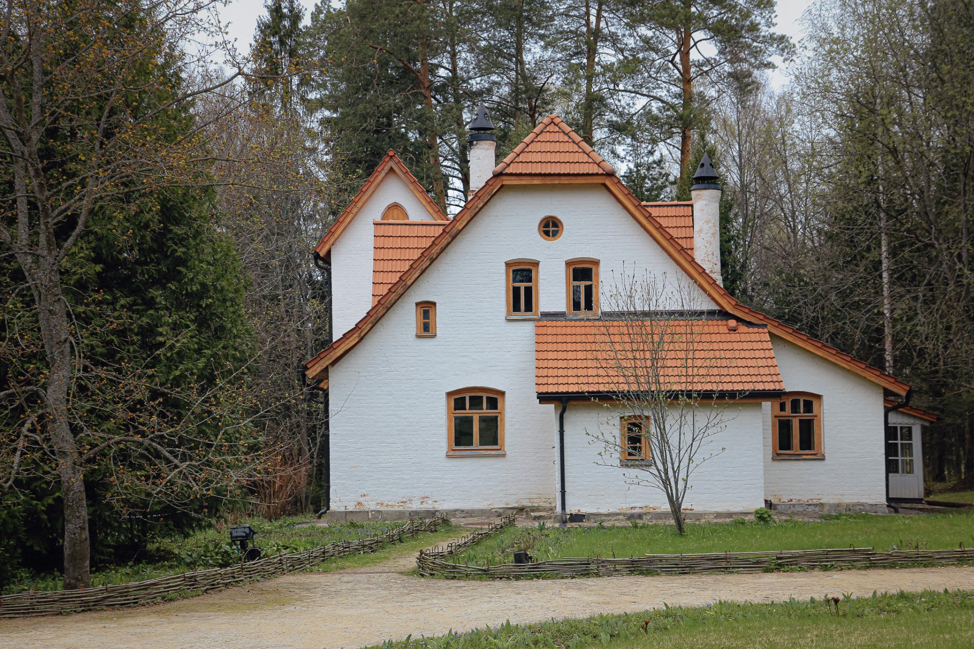 Wit huis met oranje dak, omgeven door bomen.