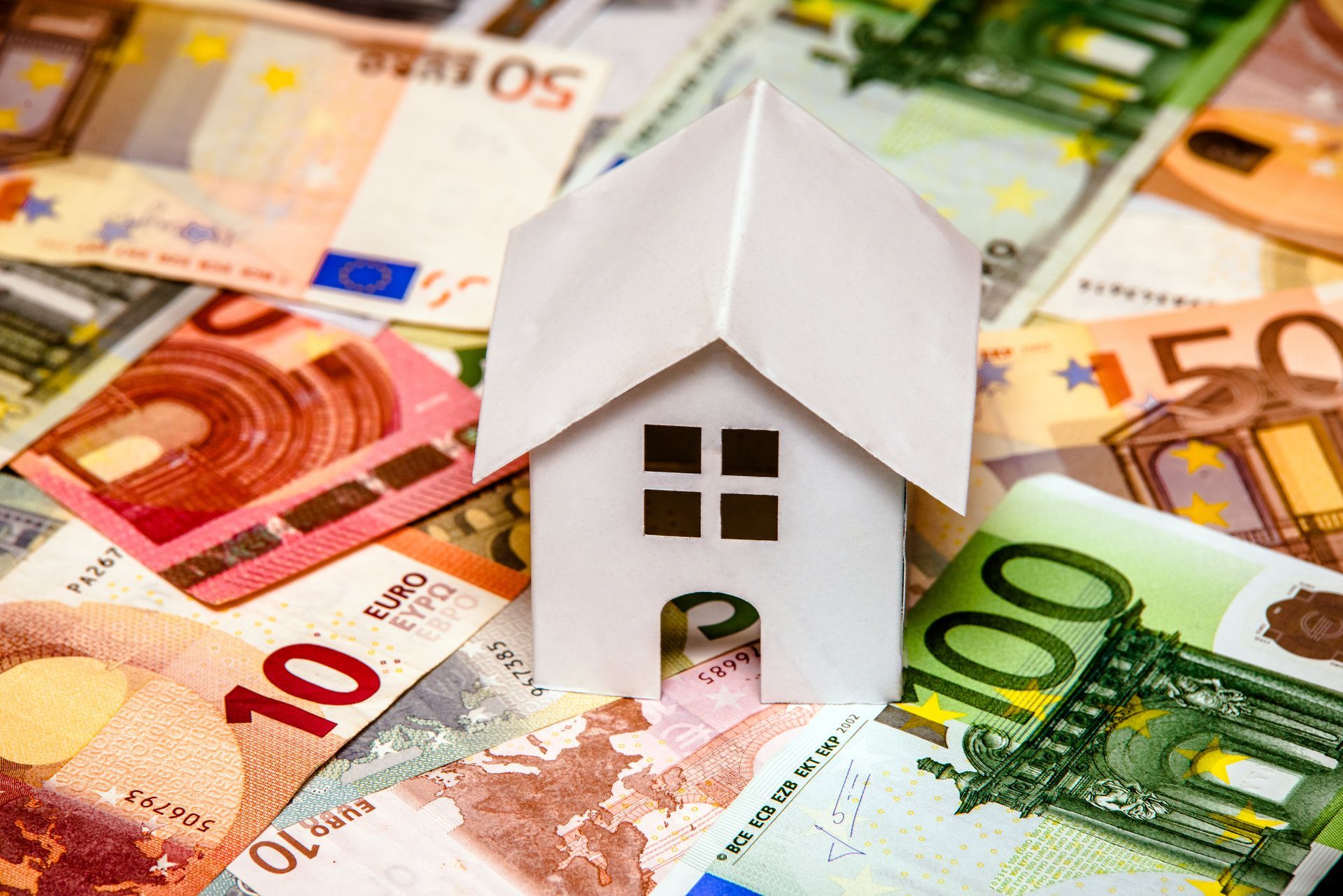 Model van een wit papieren huis bovenop eurobankbiljetten.