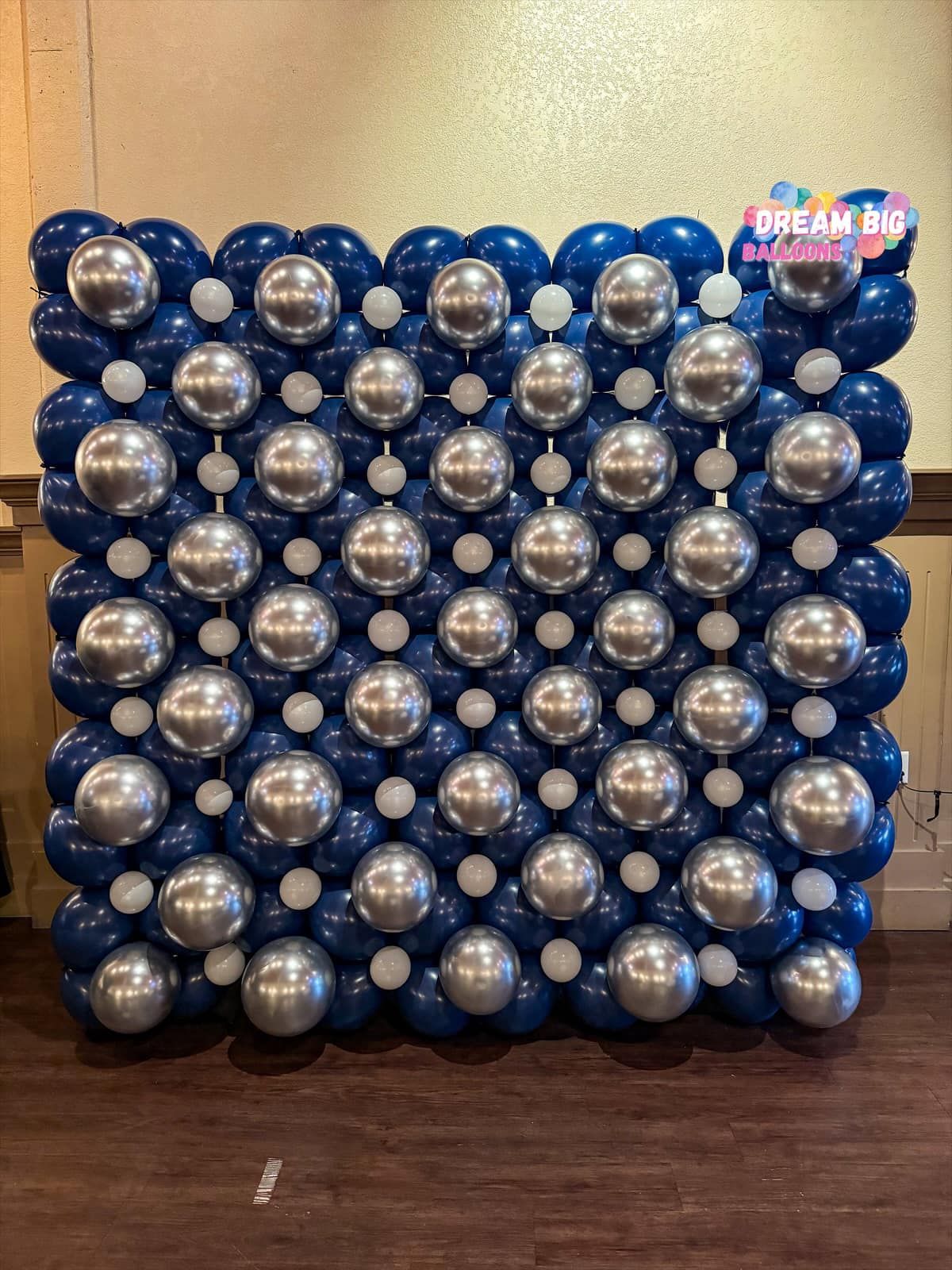 A wall made of blue and silver balloons on a wooden floor.