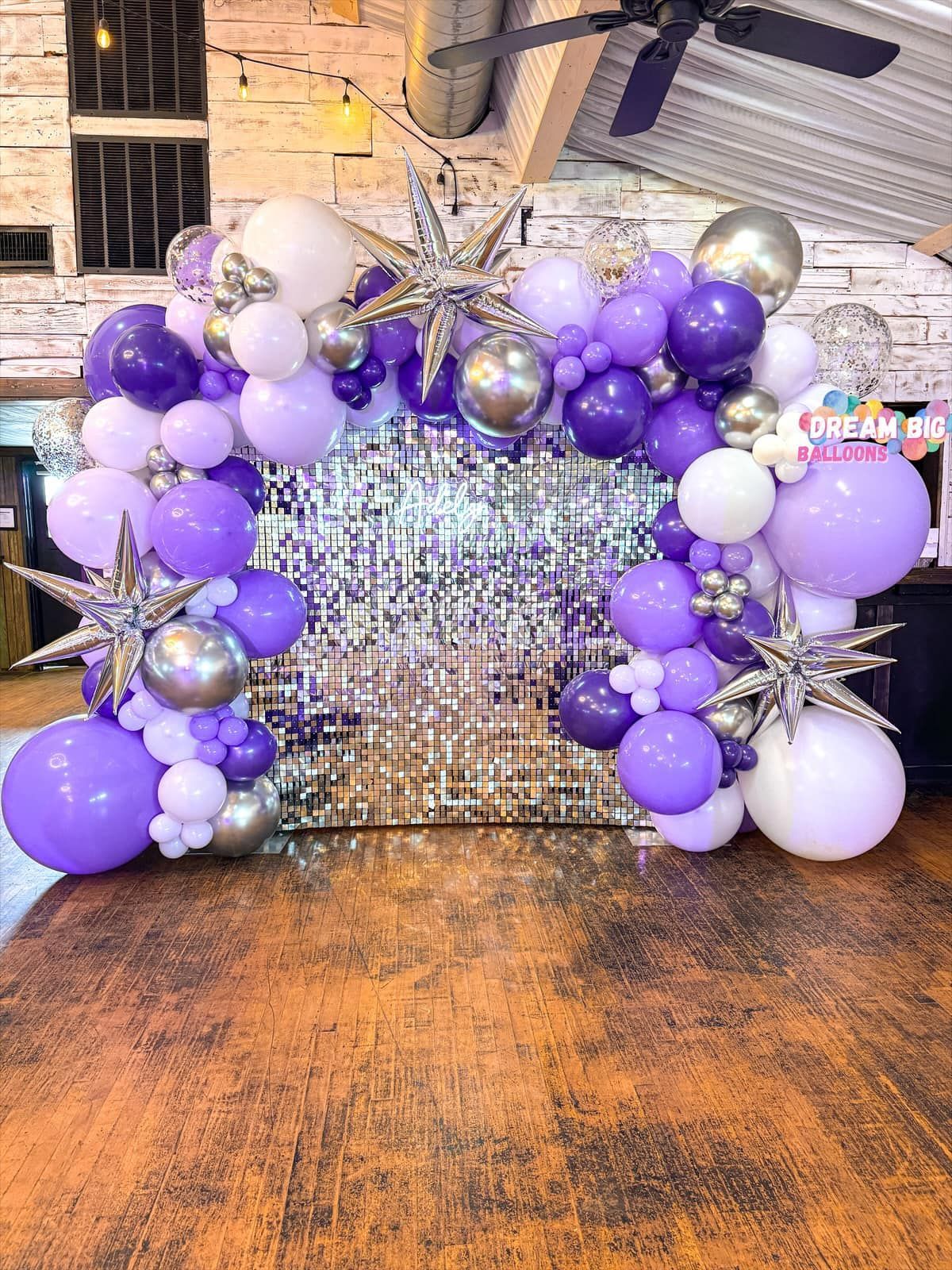 A bunch of purple and white balloons are sitting on a wooden floor.
