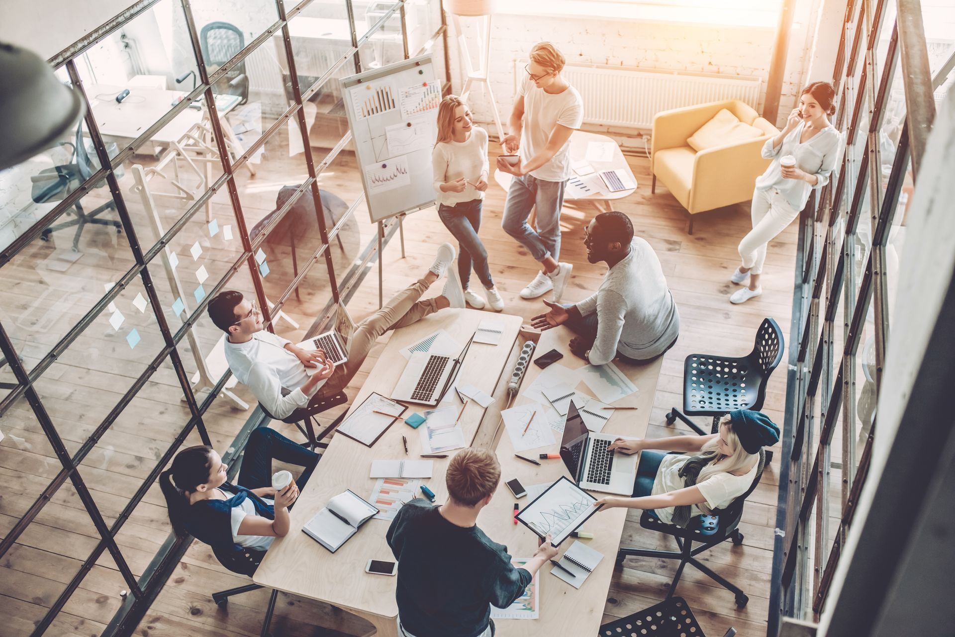 Des personnes travaillent ensemble dans un bureau moderne, autour d'une table et d'un tableau blanc.