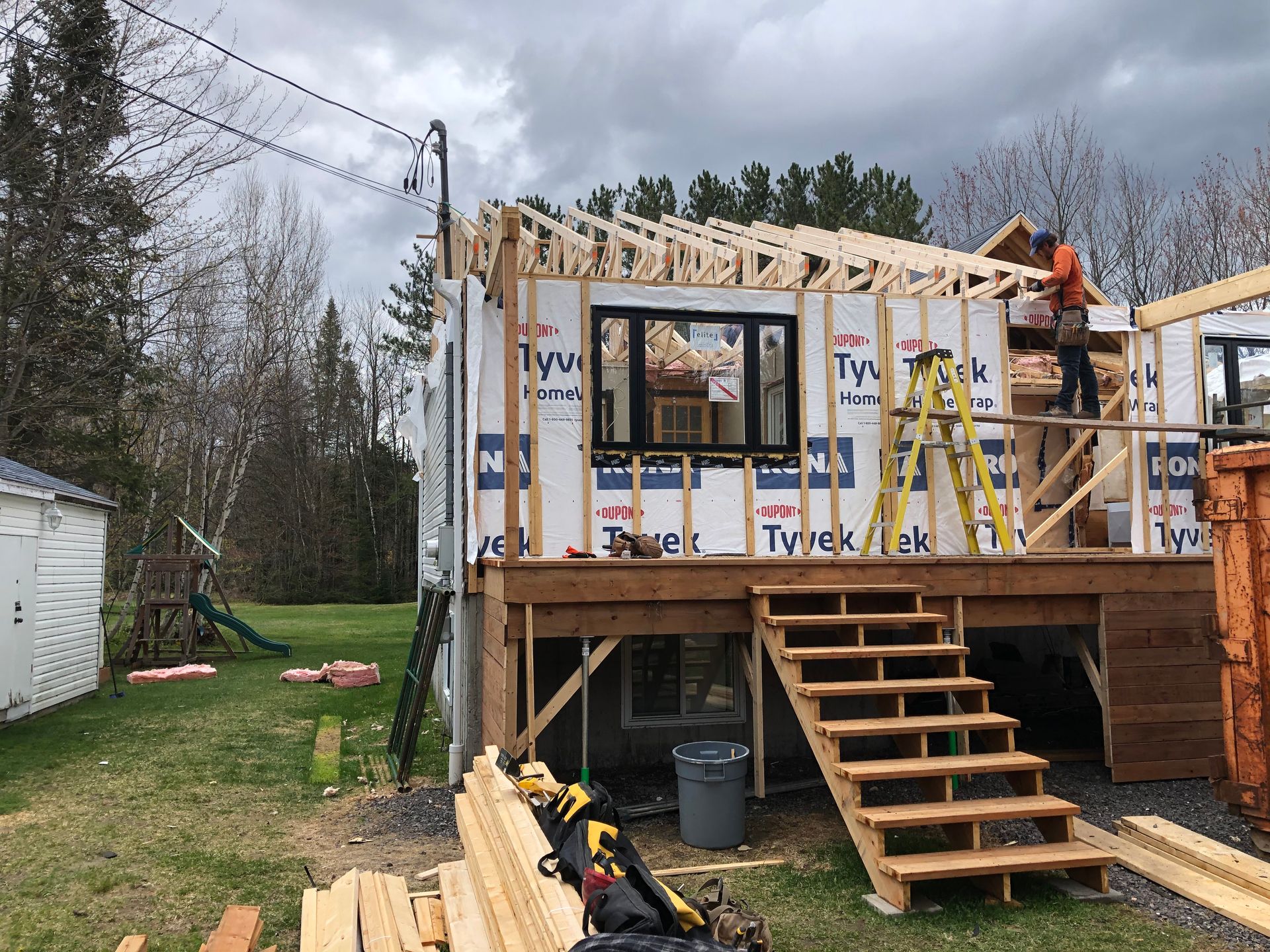 Maison en construction avec un ouvrier sur la terrasse, charpente en bois, nouvelle charpente de toit, ciel nuageux.