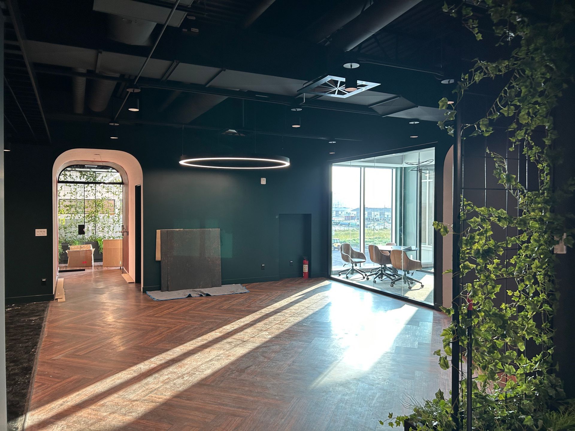 L'intérieur d'un bureau vide, avec des murs sombres, un parquet et de grandes fenêtres donnant sur l'extérieur.